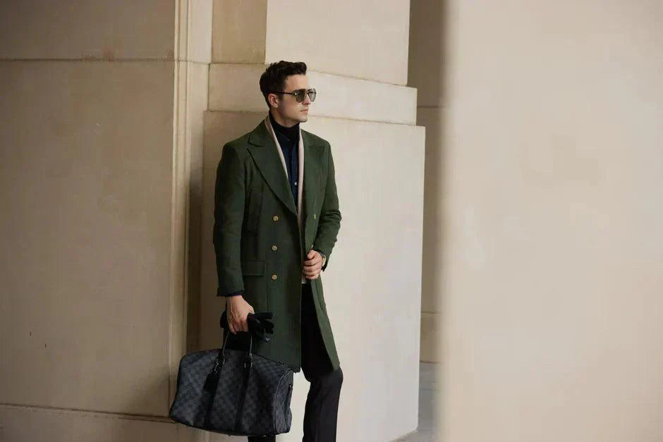 Stylish man wearing a long coat with sunglasses and a designer bag in an urban setting