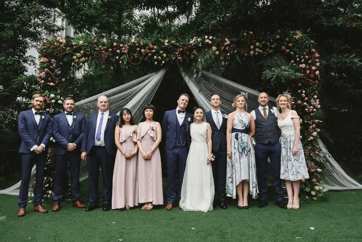 Group of wedding guests in stylish wedding suits for men posing near a floral backdrop