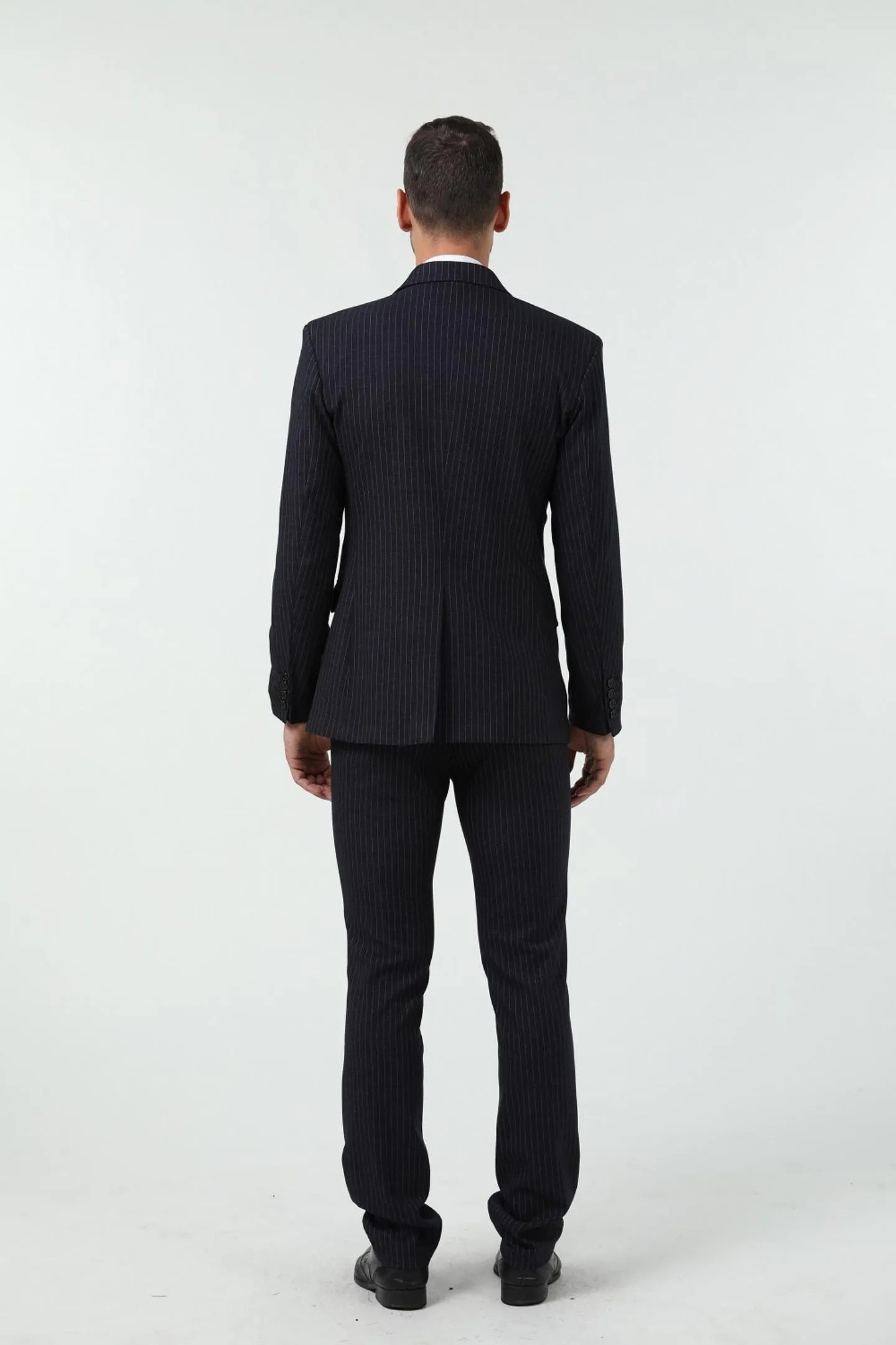 back view of a man in a black slim fit pinstripe 3 piece suit, showing the suit’s details and slim fit silhouette.