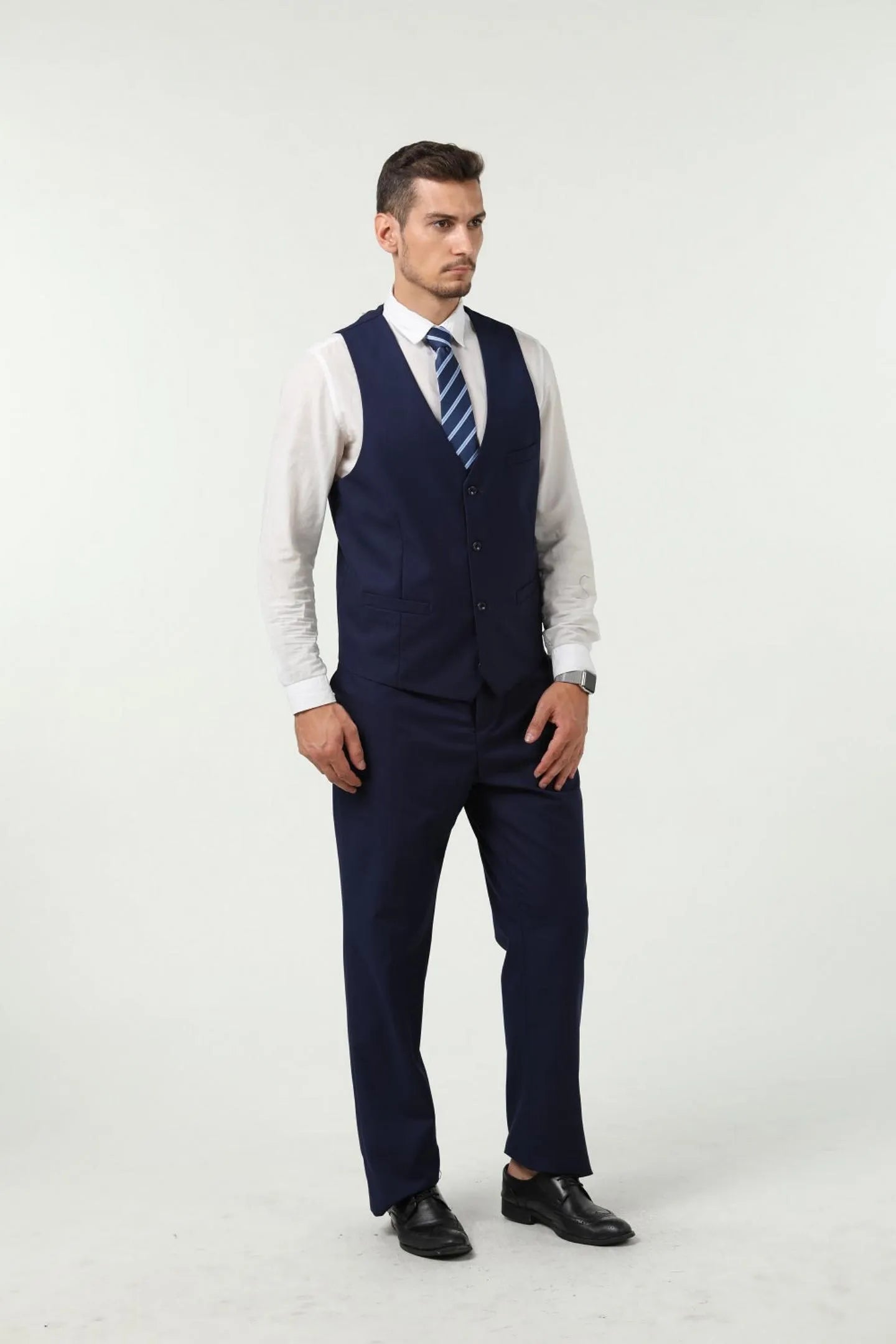 close-up view of model in a navy blue men's vest, paired with a slim fit 3-piece suit and a blue striped tie.