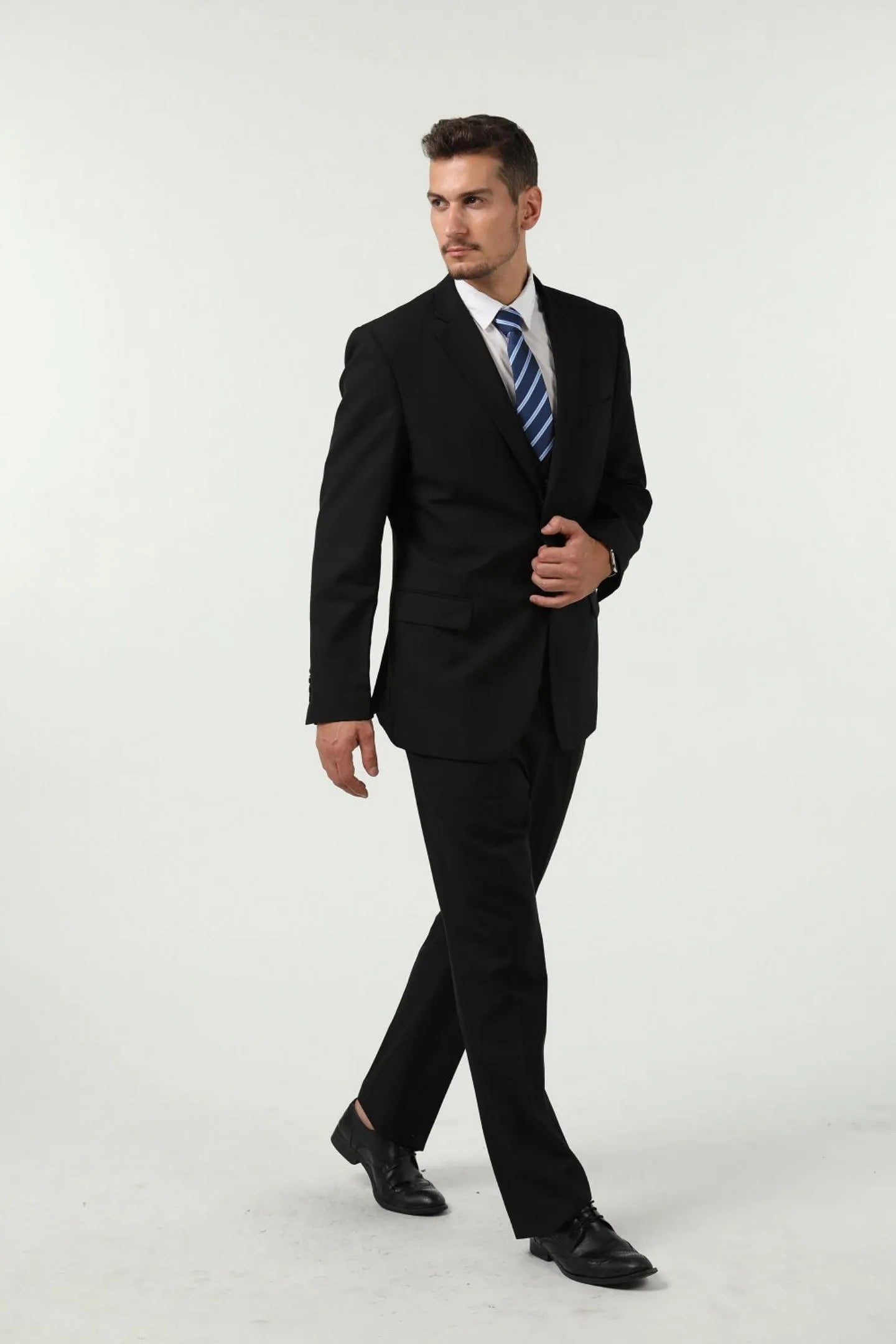 full front view of a man in a slim-fit black two-button 3-piece suit, paired with a blue striped tie and black dress shoes, exuding professional elegance.