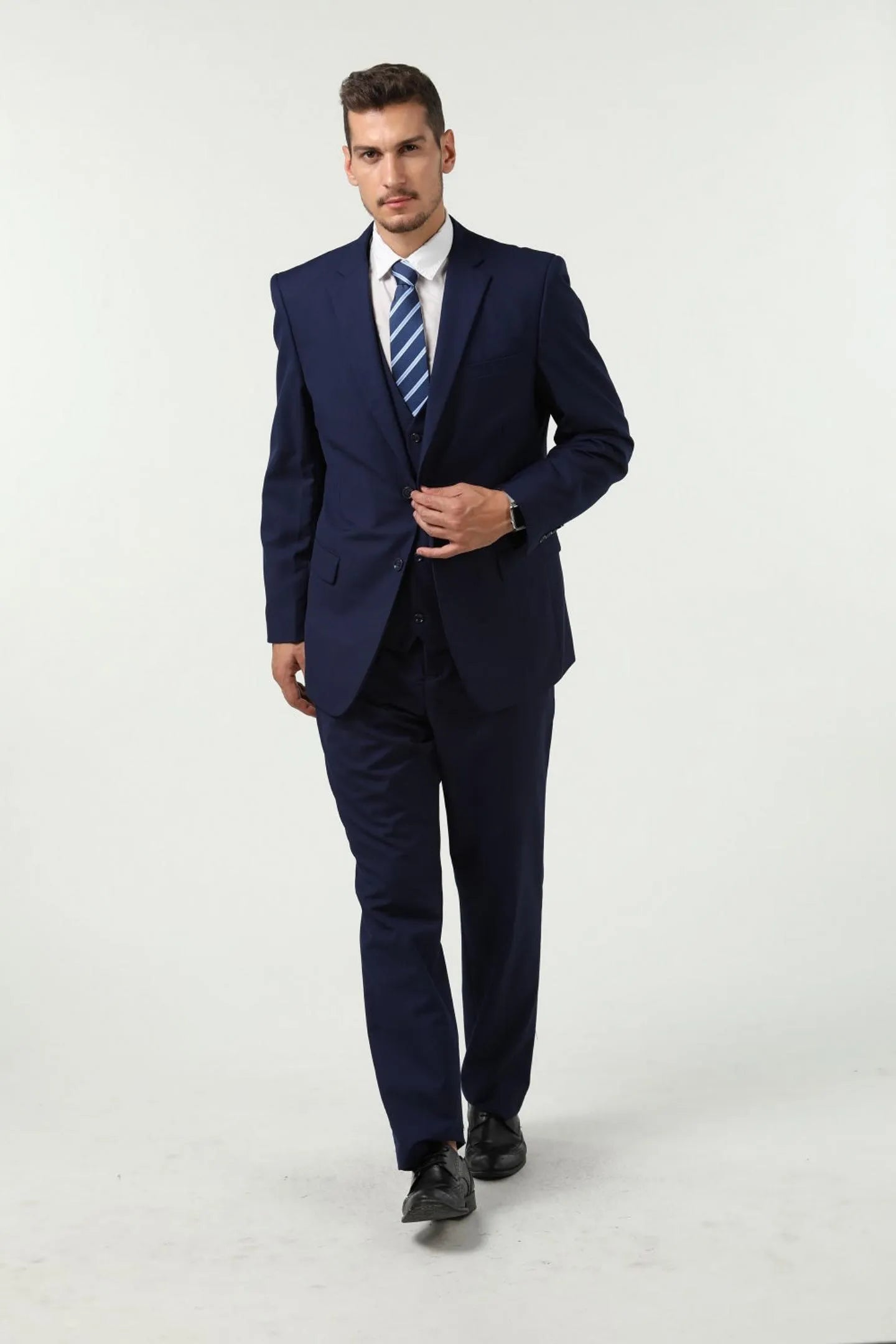model wearing a navy blue men's slim fit 3-piece suit with two buttons, walking with confidence.