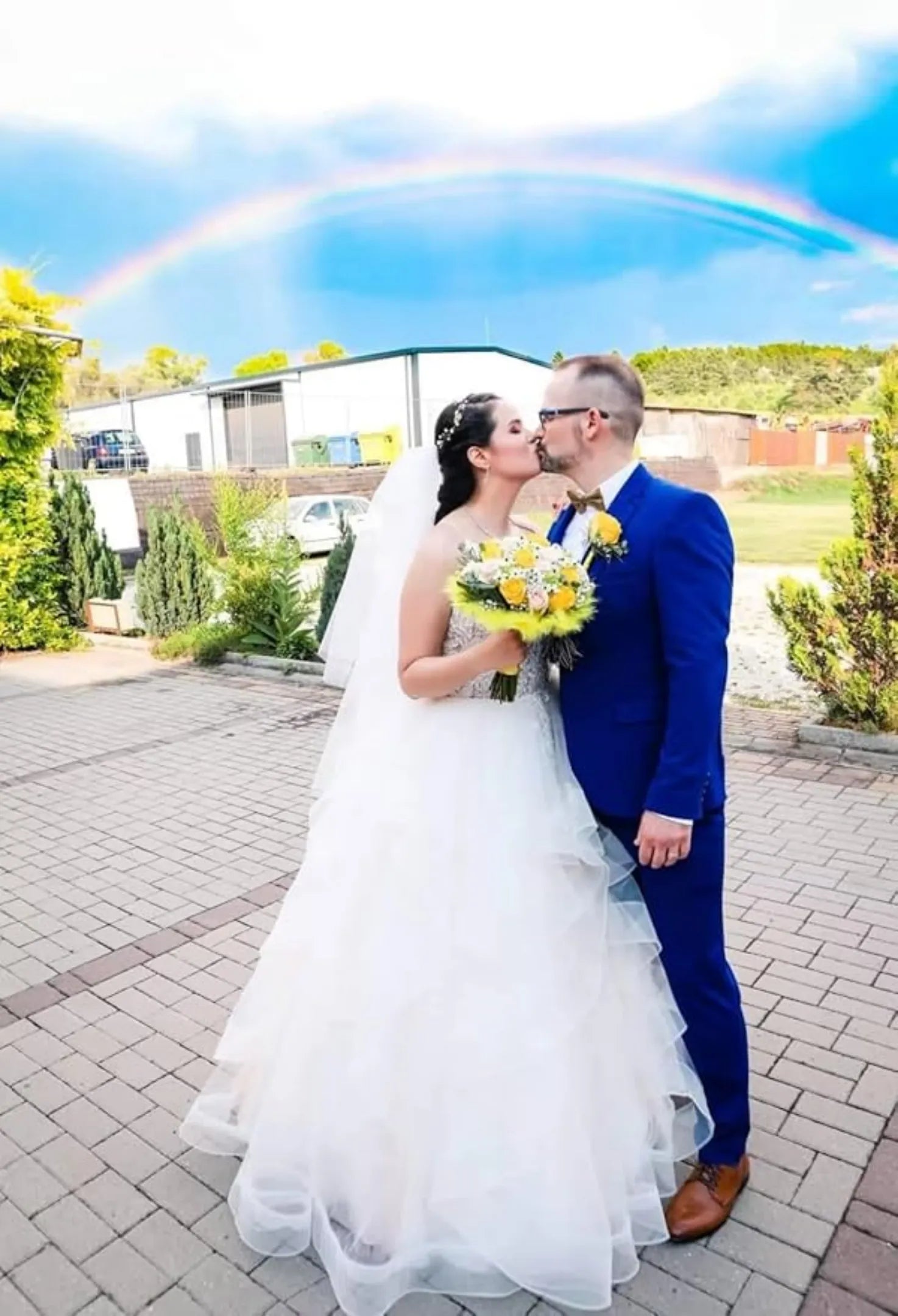 couple kissing under rainbow at wedding, groom in royal blue formal suit with yellow floral accents
