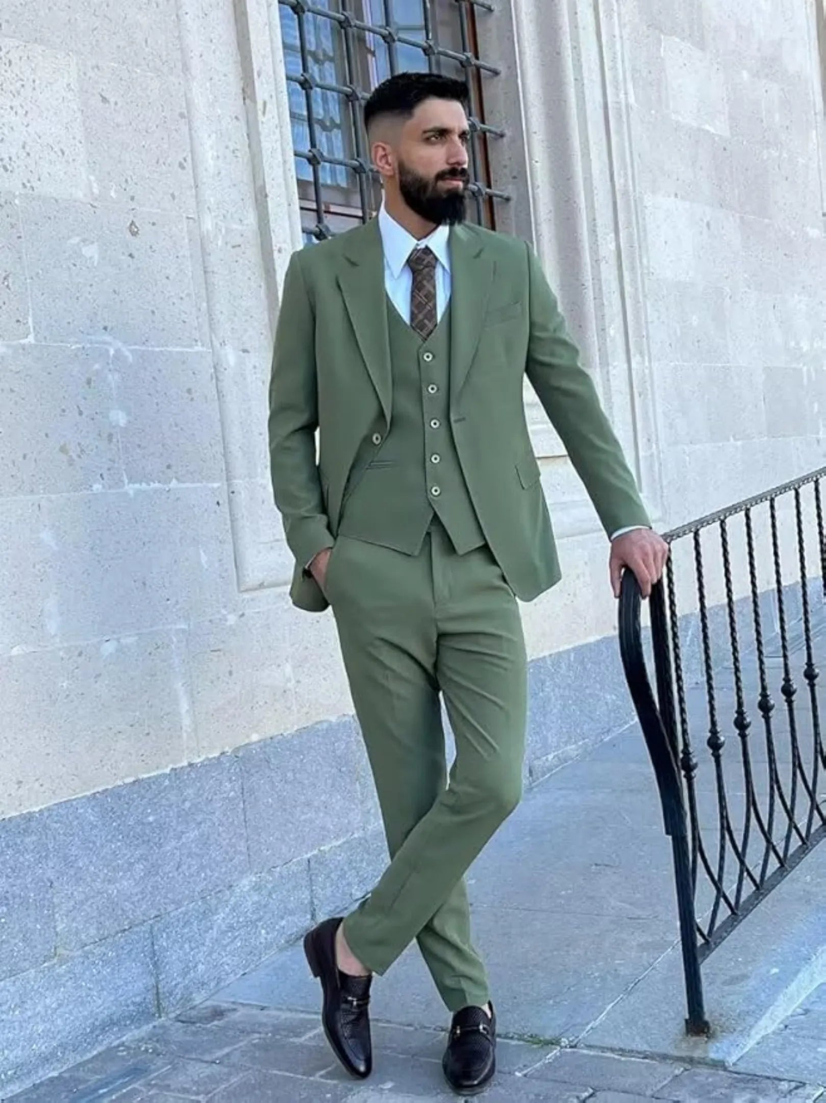 man in sage green 3 piece groom suit posing in front of stone wall with relaxed formal style