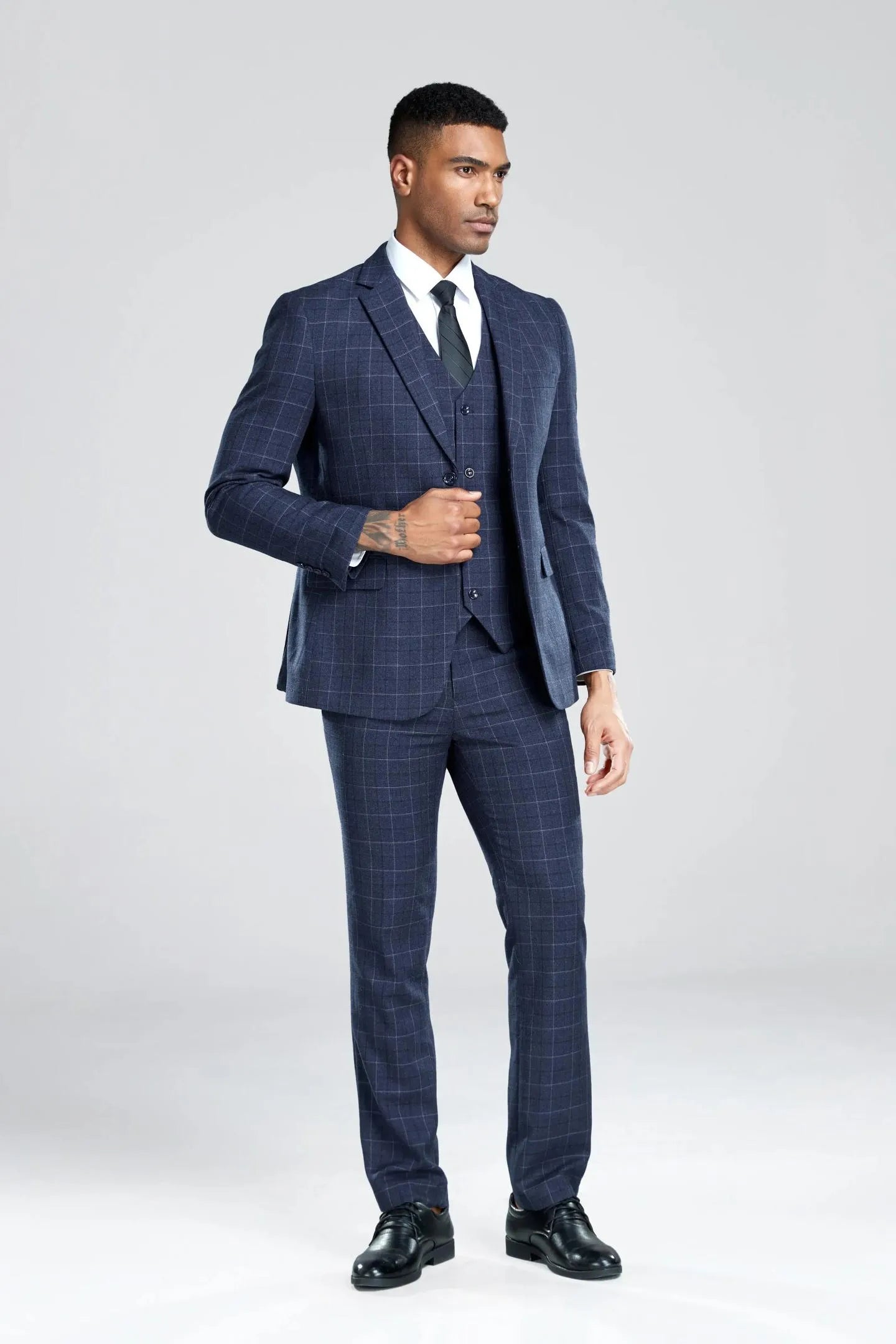 navy plaid 3-piece suit, front view with hands in pockets, black tie adding a touch of style.