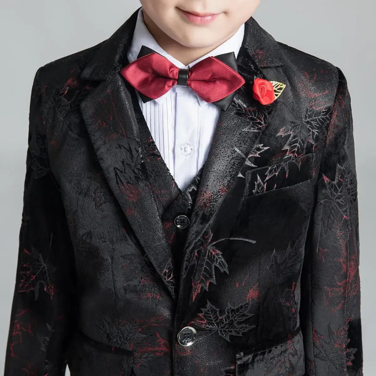Close-up of boys' black floral blazer with red rose lapel pin and satin bow tie, ideal for graduation or formal event