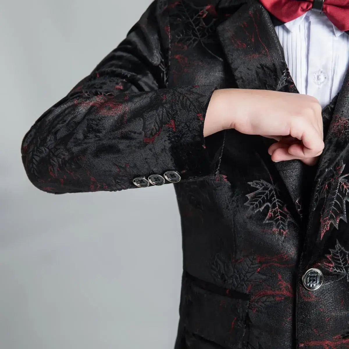Detailed sleeve view of boys' black floral suit jacket with red accents and four decorative buttons, stylish formalwear