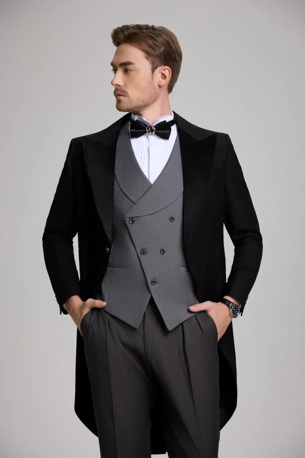 Side profile of a man's formal evening suit, showing the velvet peak lapel on the black tailcoat and the grey vest.