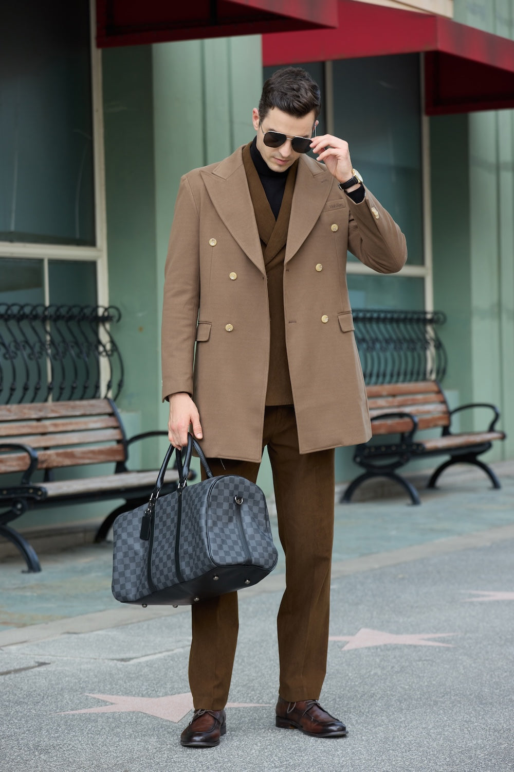 Men's coffee wool overcoat - double breasted long winter business coat, holding checked duffle bag in urban scene
