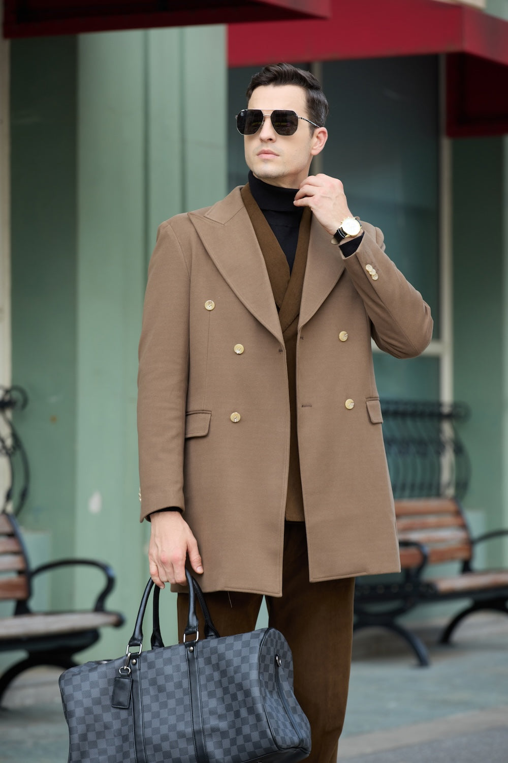 Men's coffee wool overcoat - front view of double breasted long winter business coat with gold buttons, holding checked bag in urban scene