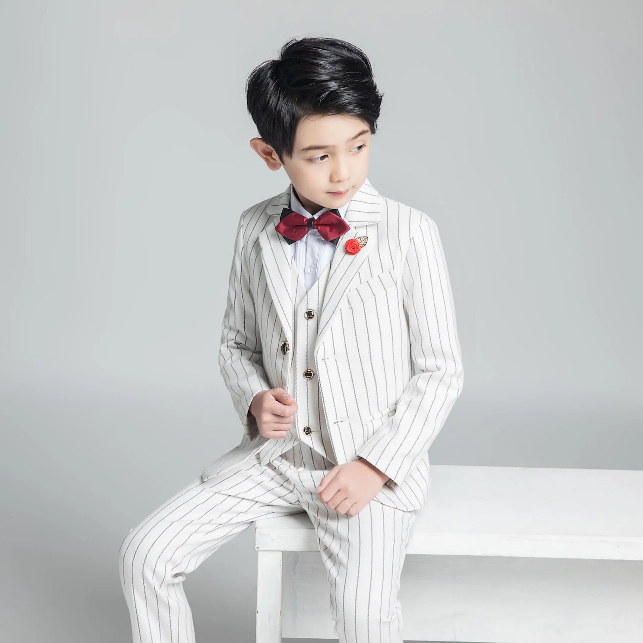 Sitting pose in boys white striped formal suit with vest and red bow tie