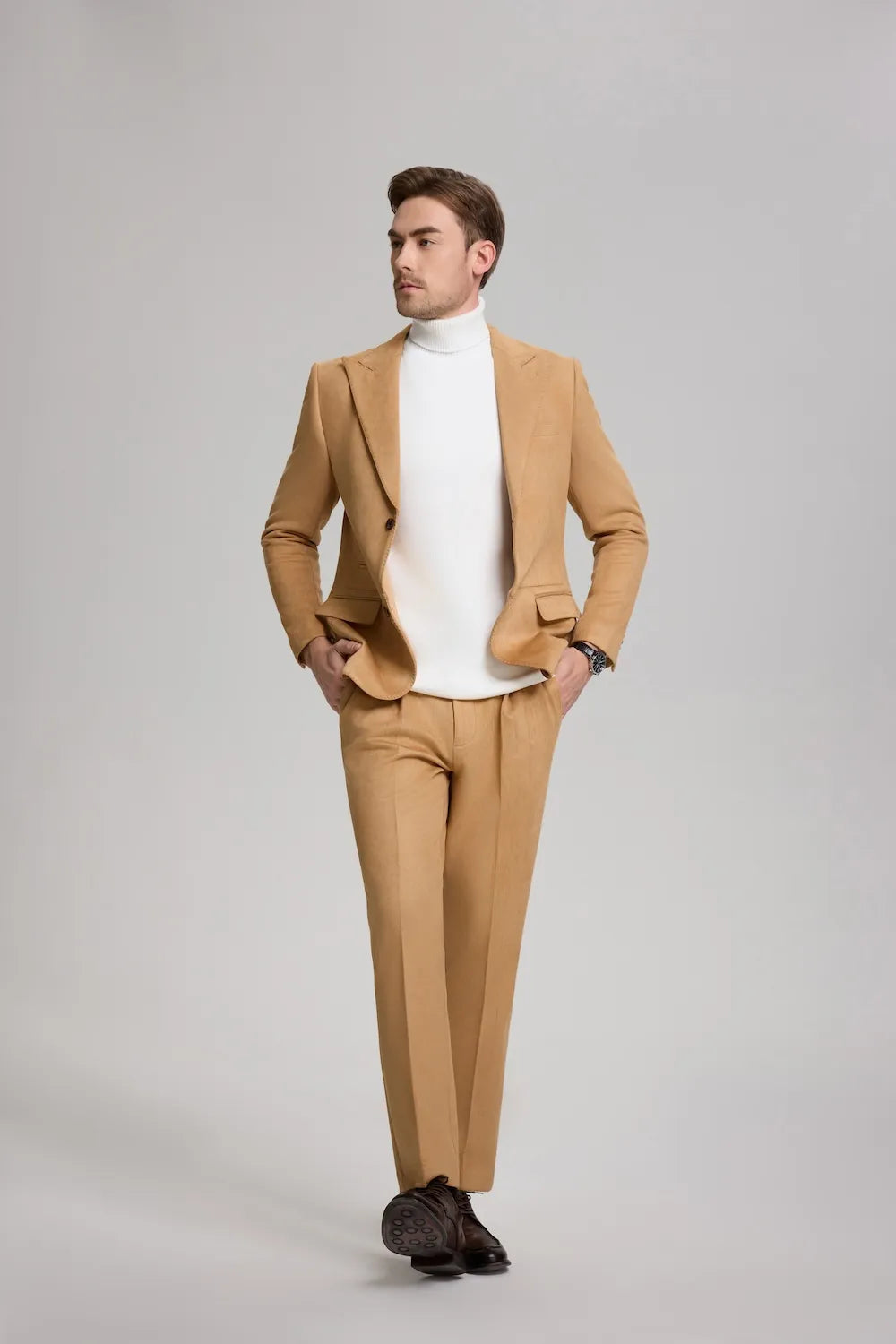 full body shot of a man walking in a light brown suede 2-piece suit with a peak lapel blazer, styled with a modern look.