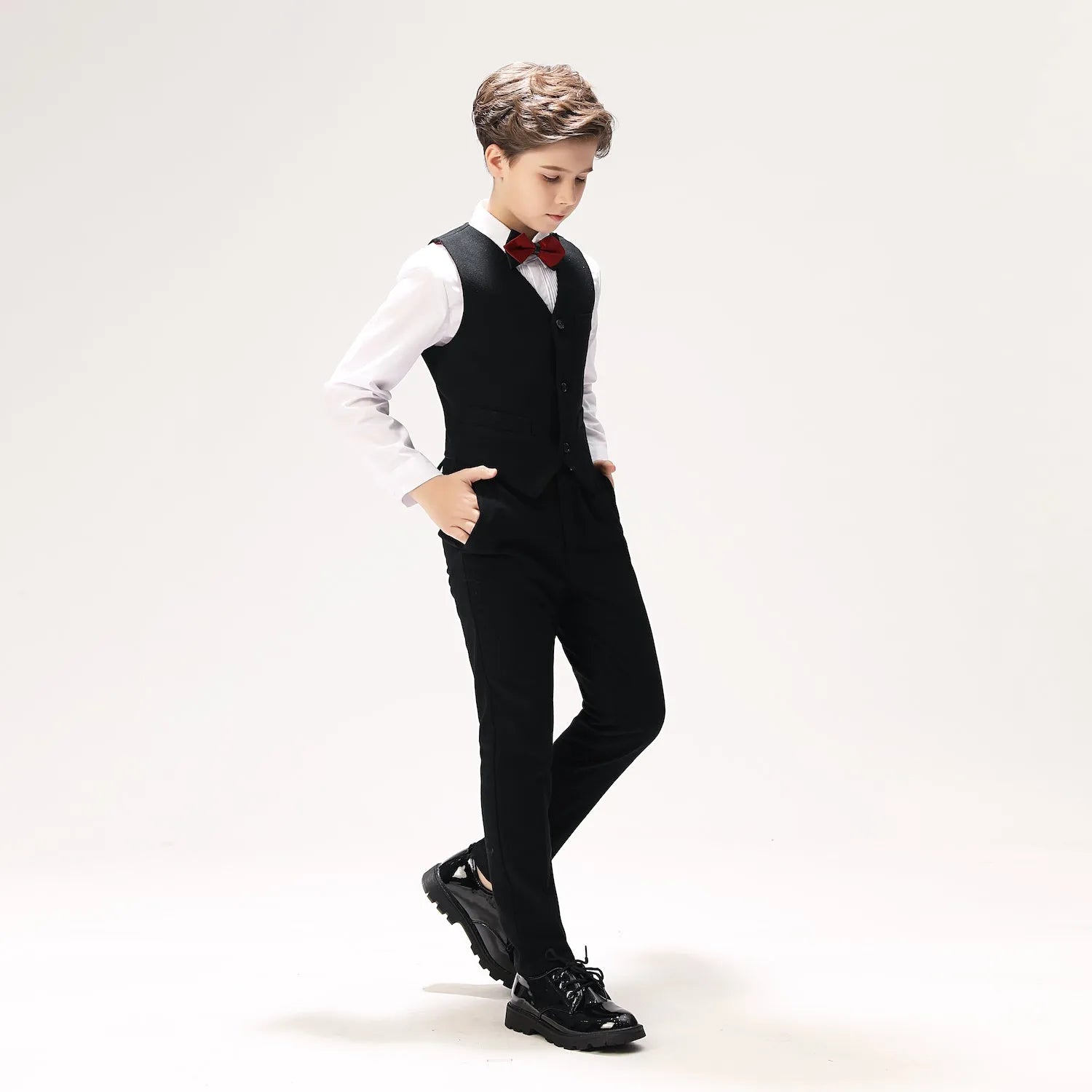 Boys' prom outfit with black vest and pants, white shirt and red bow tie, formal walking pose in glossy shoes
