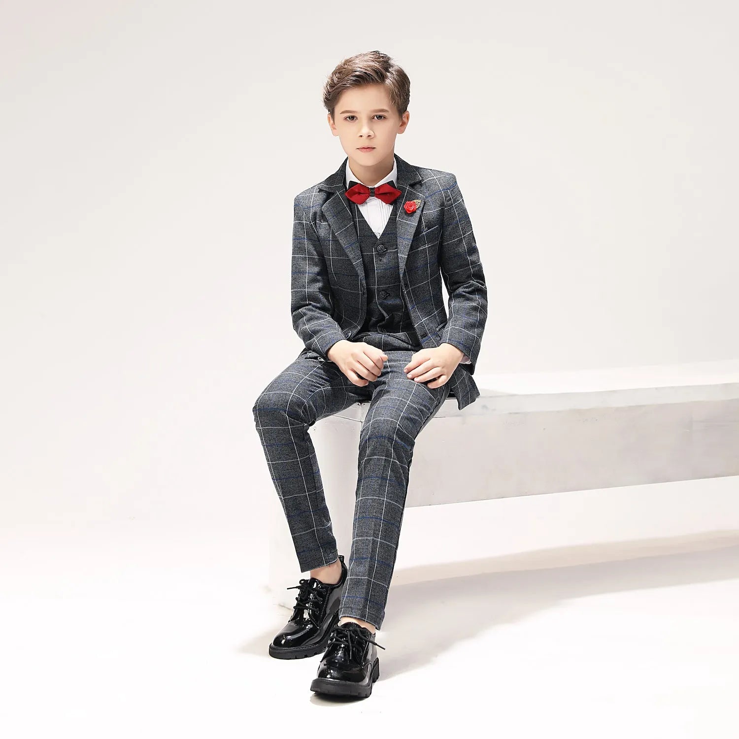 Sitting pose of boy in stylish grey windowpane plaid suit with vest and bow tie