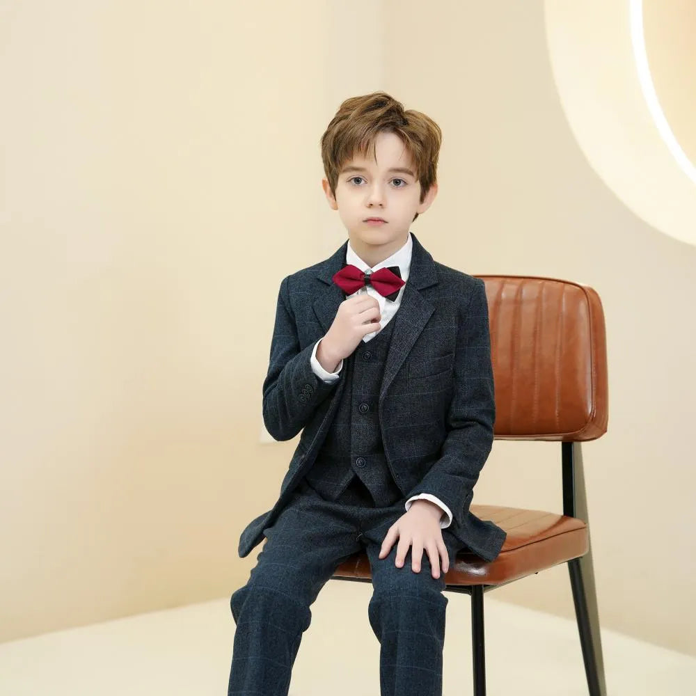 Navy plaid boys 5-piece suit: Seated boy adjusting red bow tie - elegant formal style