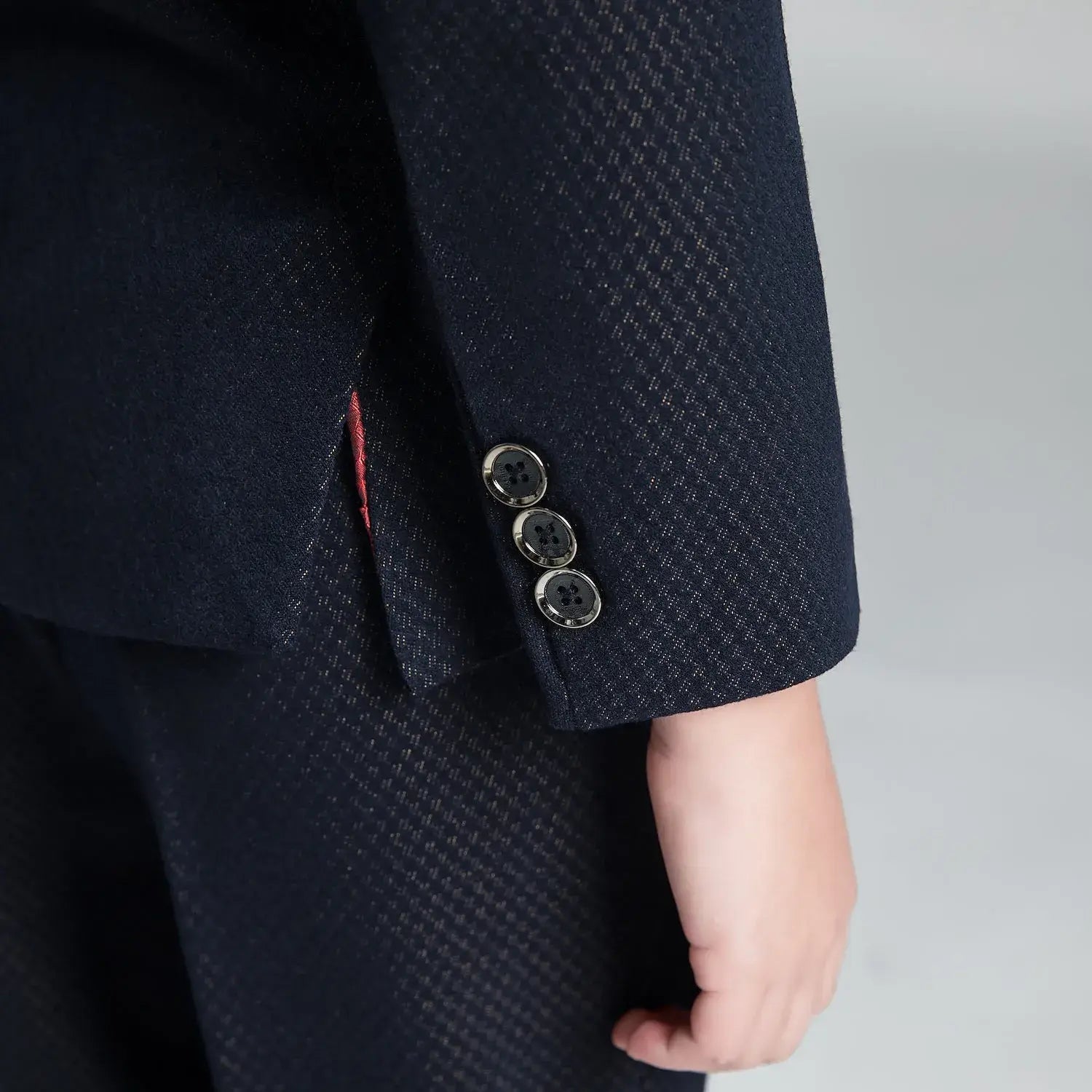Close-up of boys' navy suit cuff with textured fabric and polished three-button detail, suitable for formal holiday events