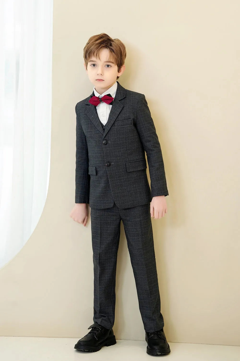 Young boy in black plaid tuxedo-style 5-piece suit with red bow tie for prom or wedding