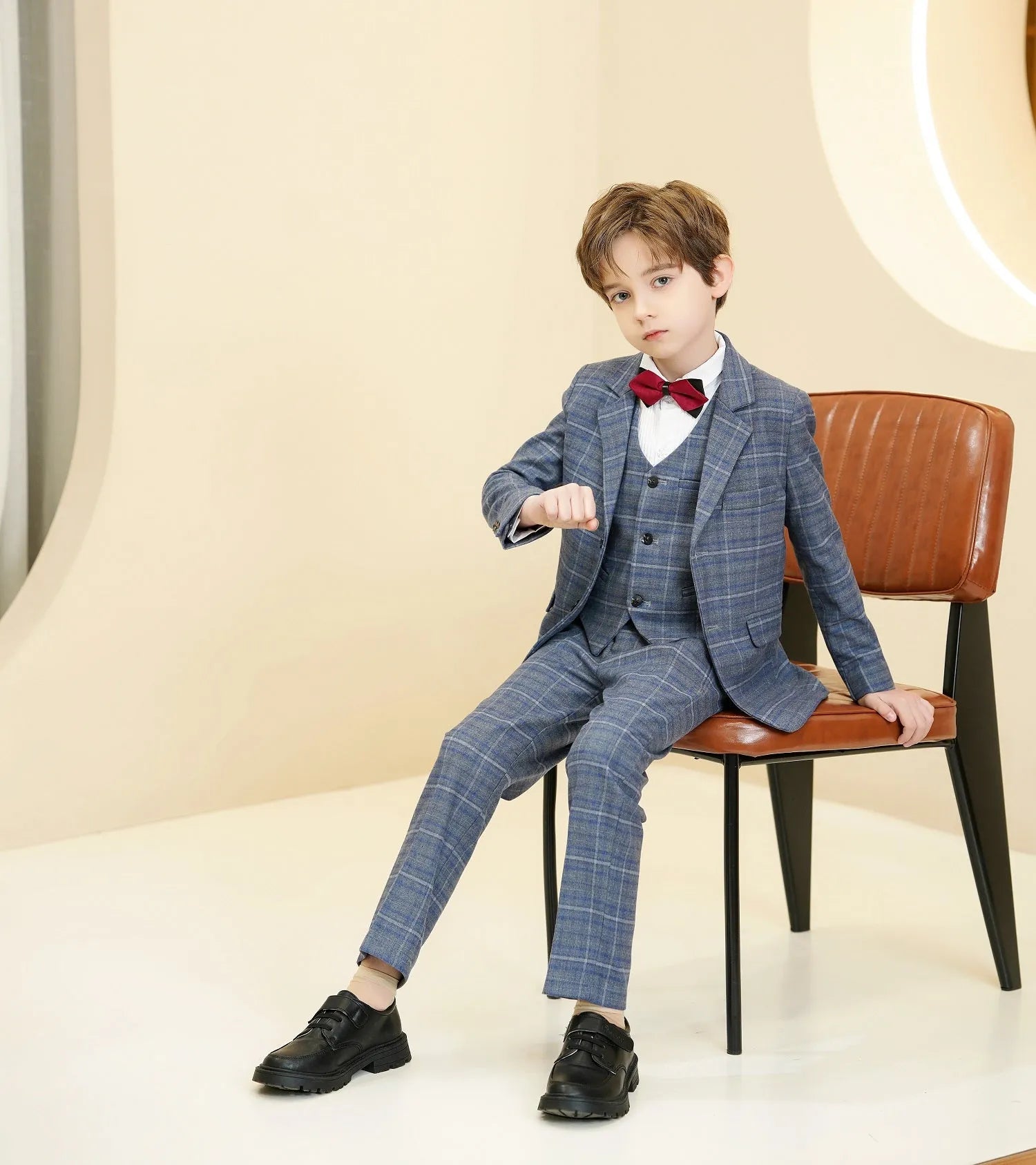 Boy in plaid 5 piece boys formal suit seated, showcasing full set with vest and bow tie.