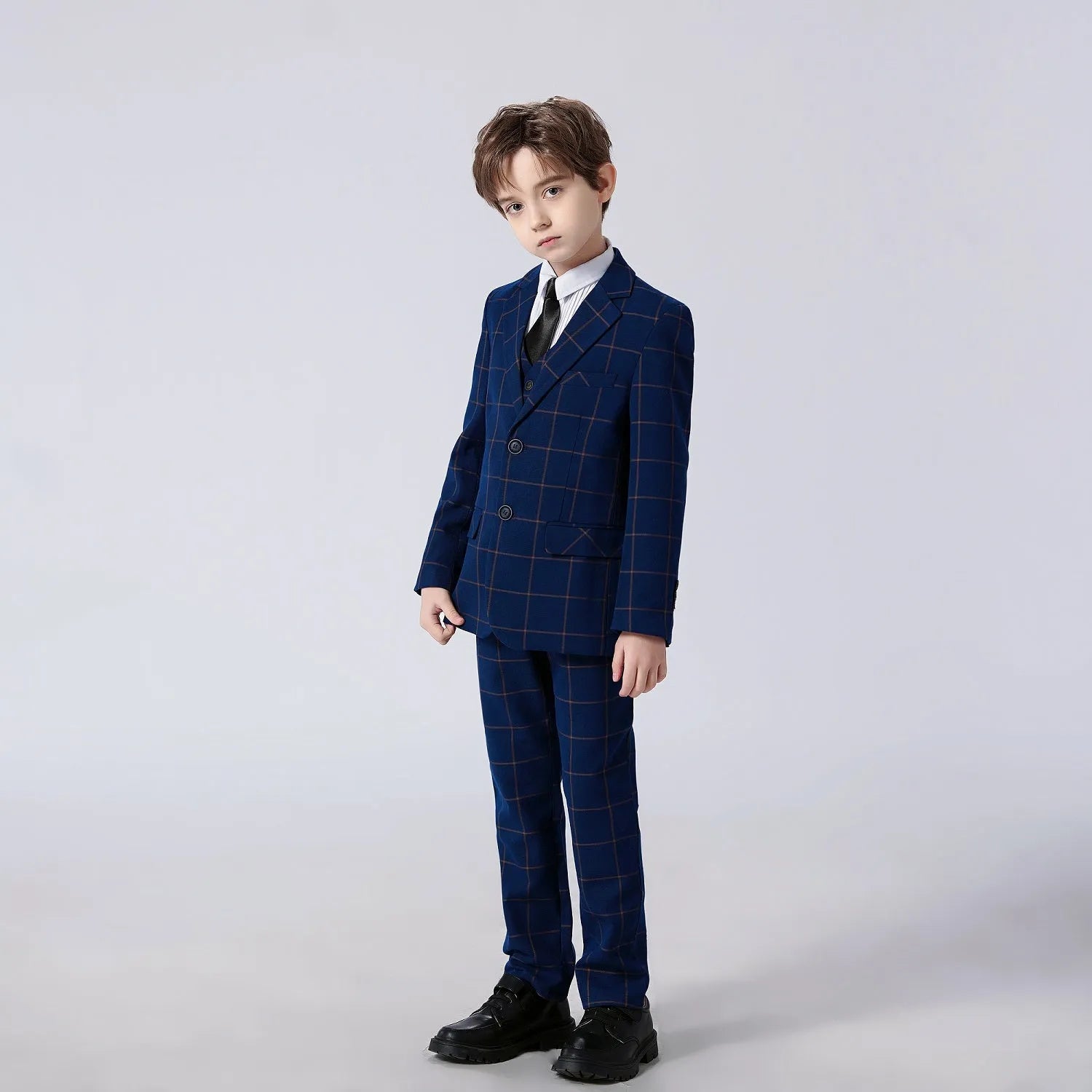 Full view of a child wearing navy checkered 5 piece boys suit with elegant striped shirt and tie.