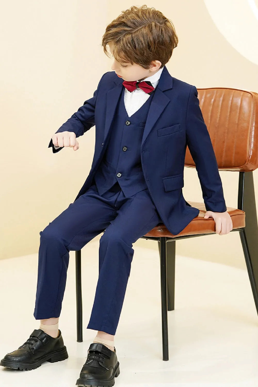 Navy formal boys' suit shown seated, complete 5-piece outfit with vest and bowtie for stylish party or banquet look