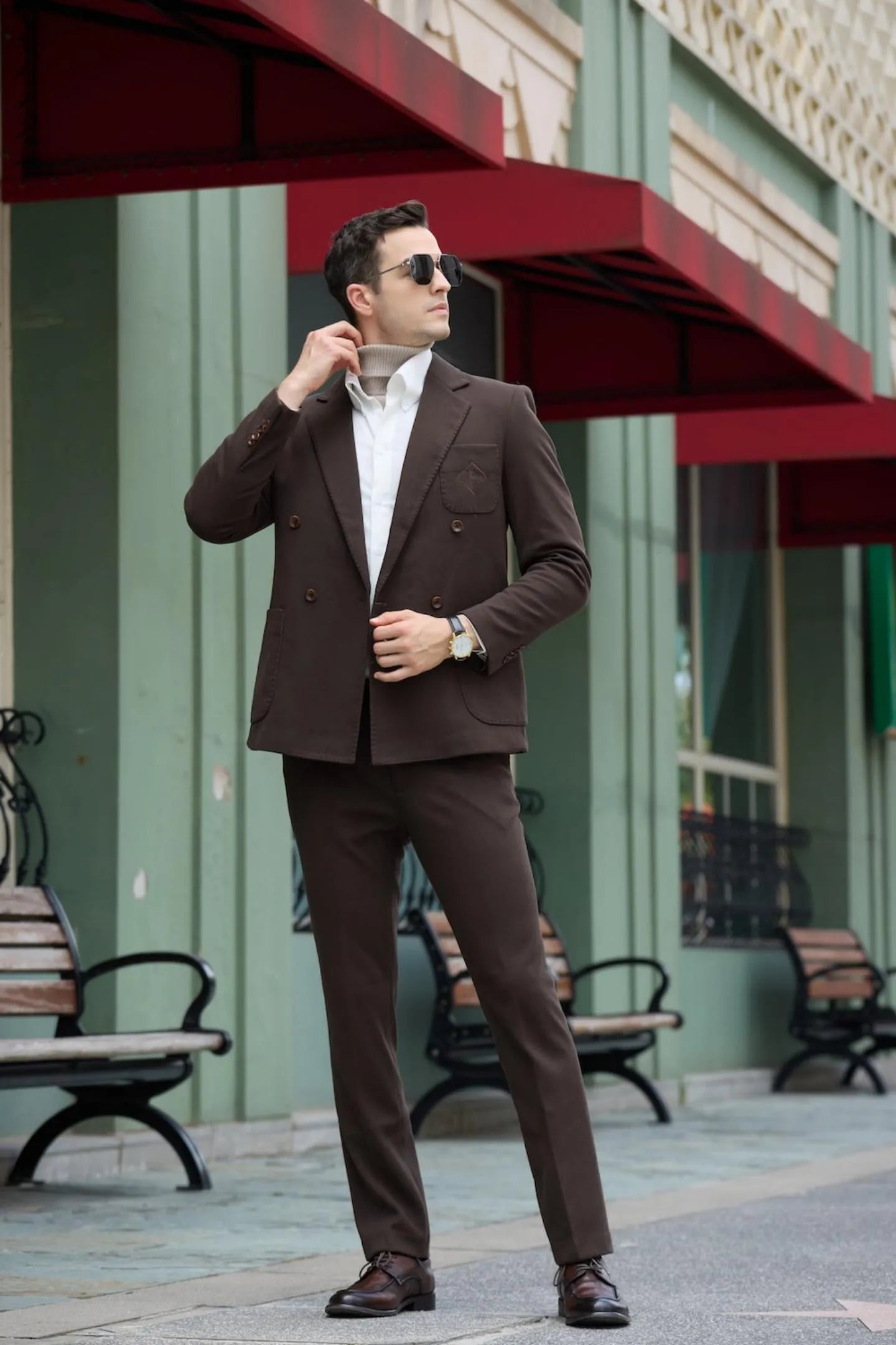 Model in coffee double breasted herringbone tweed 2 piece men's suit, standing outdoors with white shirt and brown shoes
