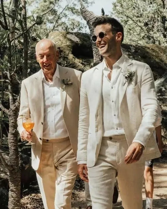 Two men in light beige linen 2 piece suits walking outdoors, styled with white shirts for summer wedding