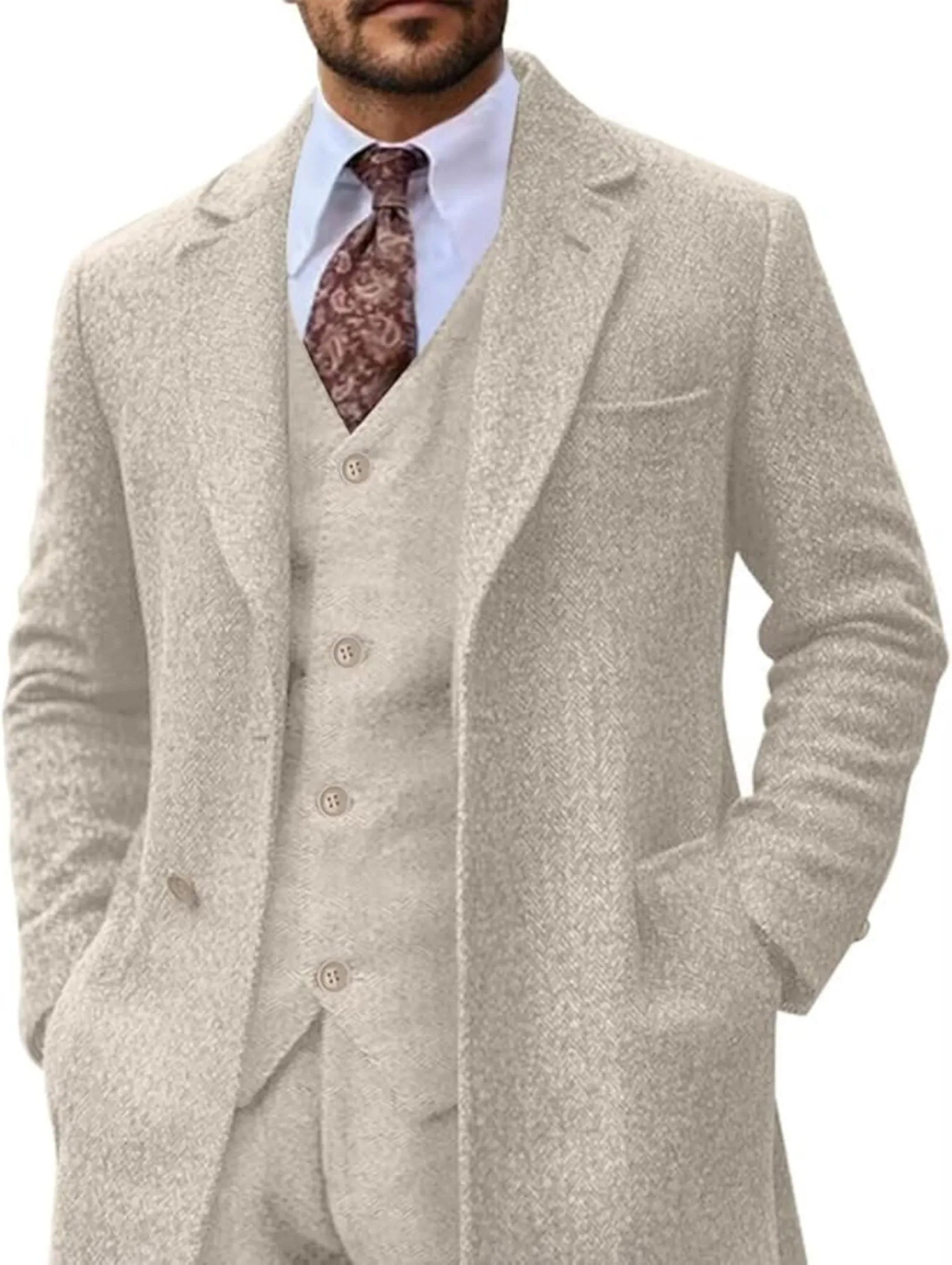 close-up front view of men's champagne herringbone 3 piece suit with long blazer, paired with white shirt and paisley tie for formal look.