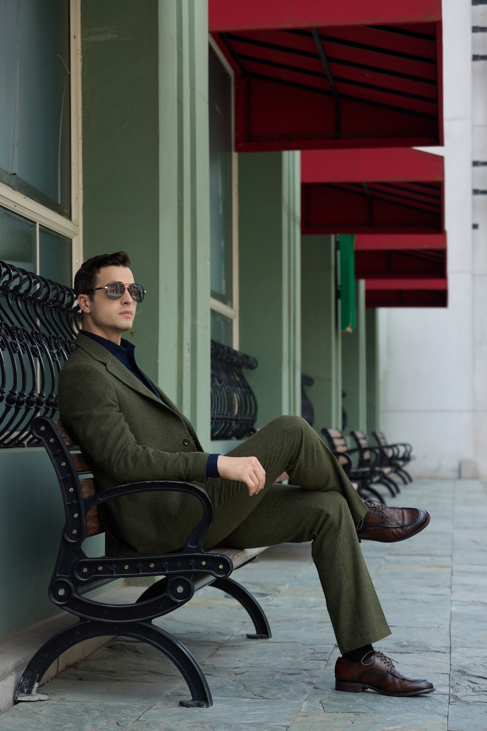 Men's green herringbone wool suit in prom style, seated pose with brown shoes