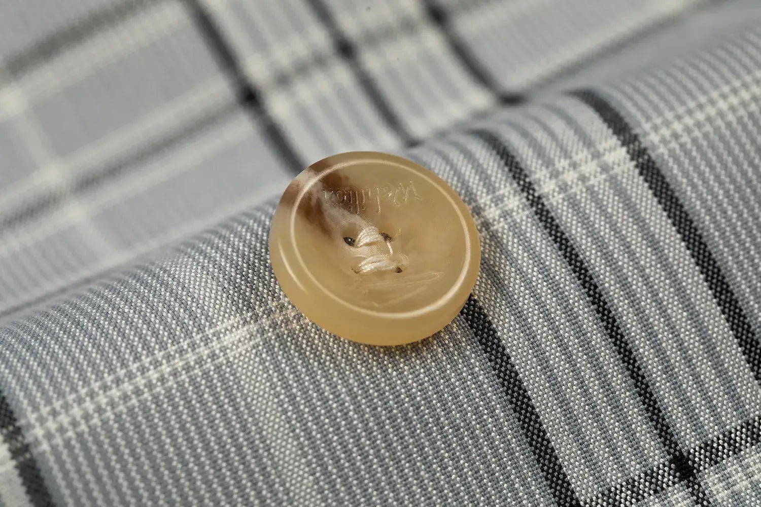 Beige button detail on grey plaid men's blazer showing stitching and texture.