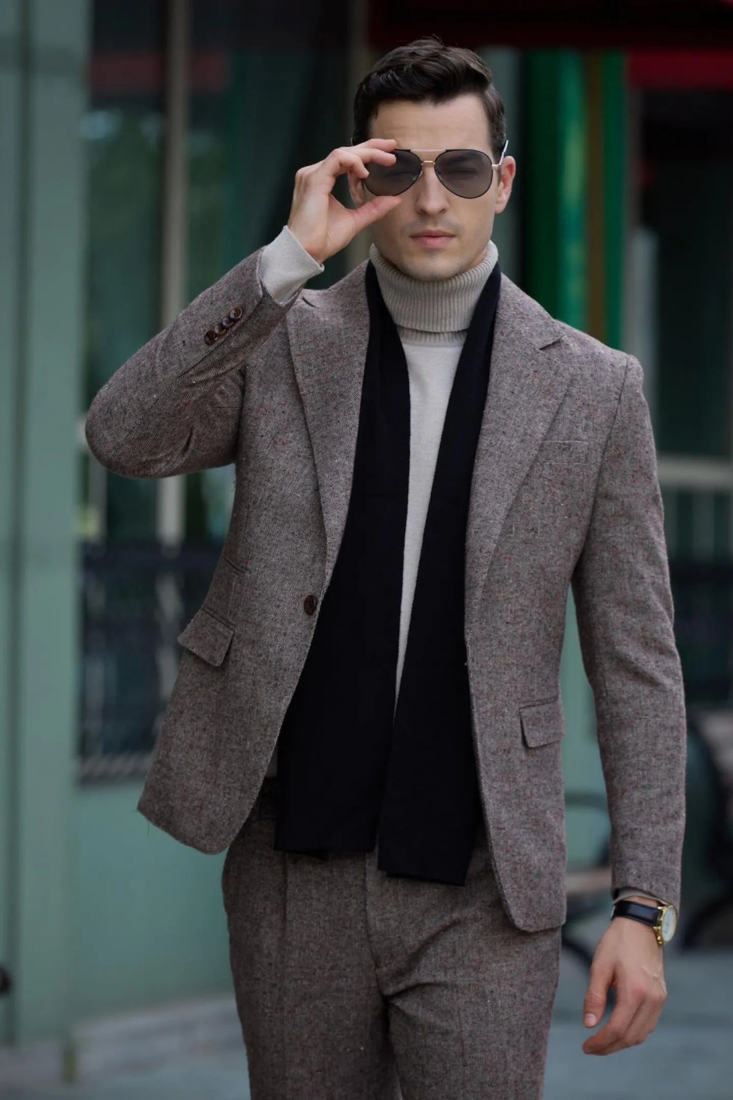 men's brown tweed herringbone 2-piece suit with black scarf, adjusting sunglasses, showcasing a business look.