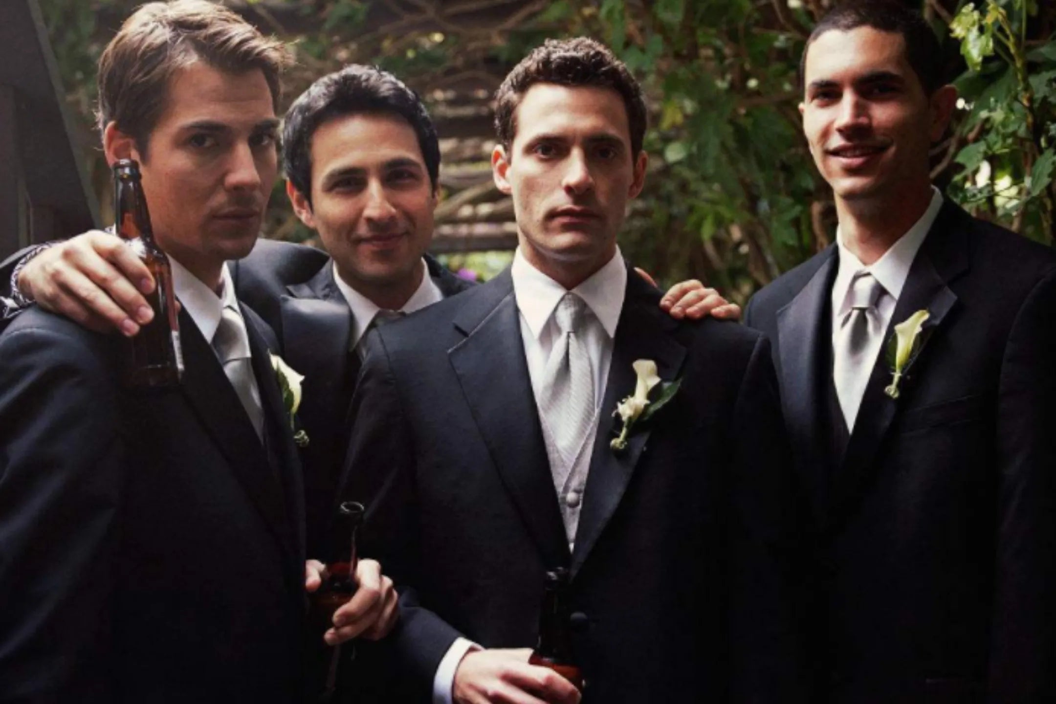 four men wearing classic black blazers with boutonnieres, styled with ties and shirts, showing modern formal blazer fashion.