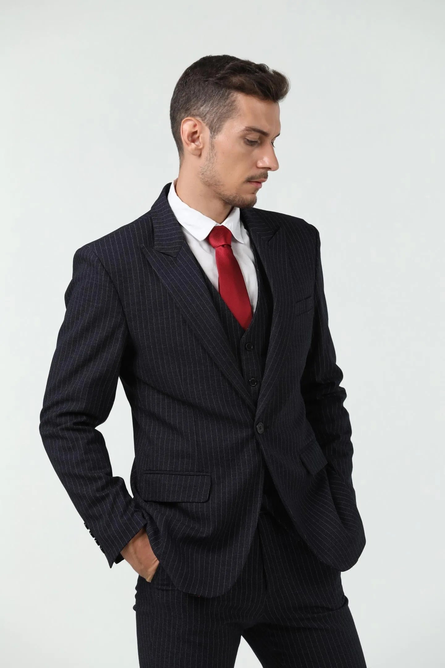 side view of a man in a black slim fit pinstripe 3 piece suit with a red tie, white shirt, and a classic business look.
