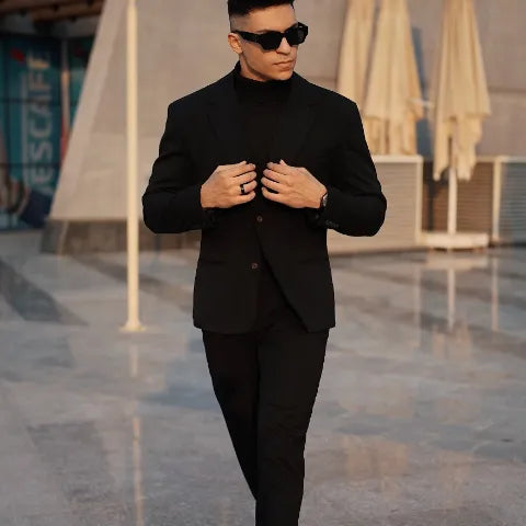Confident man in a sleek black suit and turtleneck walking through a modern plaza at sunset, exemplifying work and formalwear style.