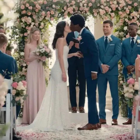 Groom in a navy wedding suit kissing the bride beneath a floral arch, flanked by groomsmen in matching blue suits during an elegant ceremony.