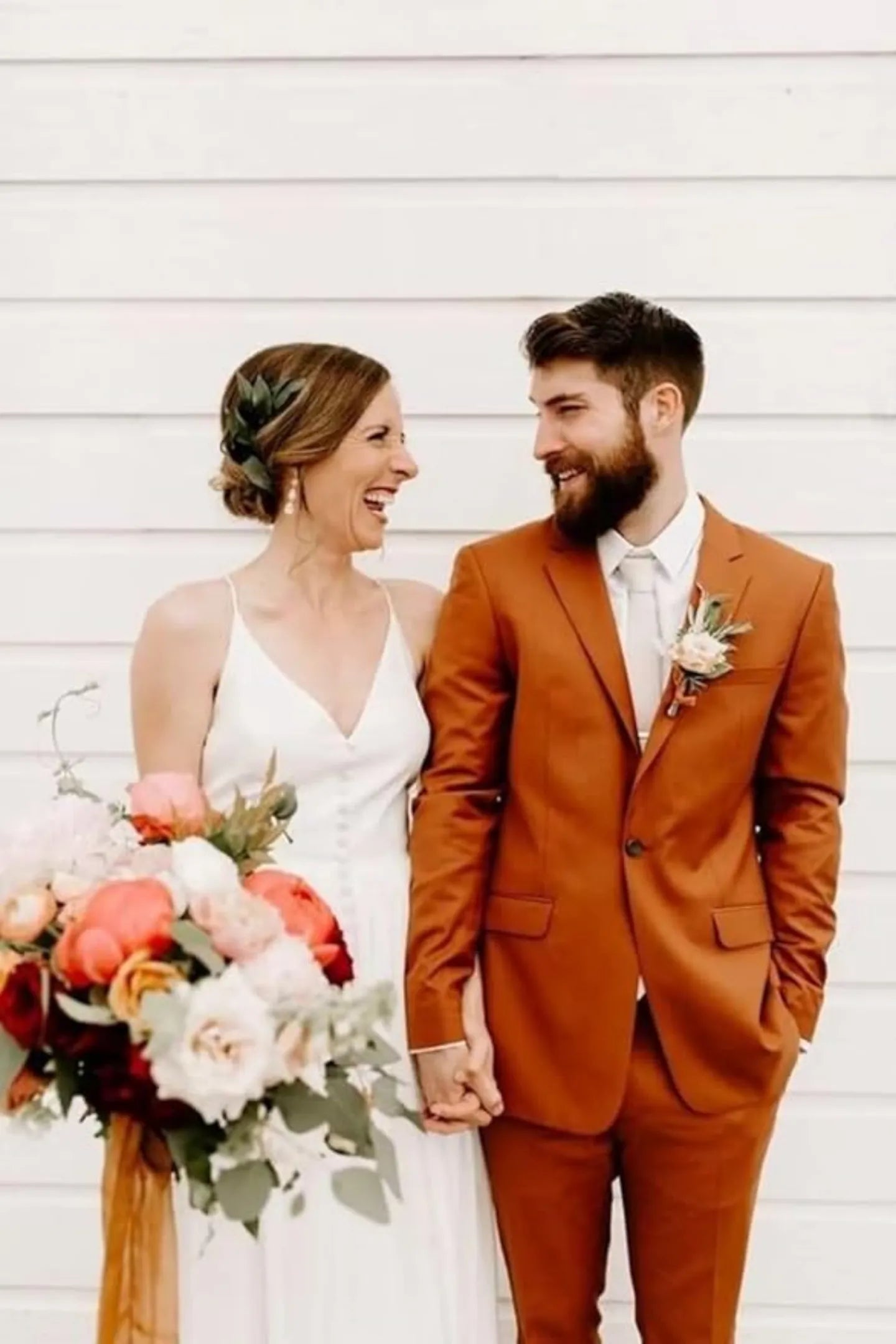 outdoor wedding with groom in burnt orange 3 piece suit and bride in white gown smiling