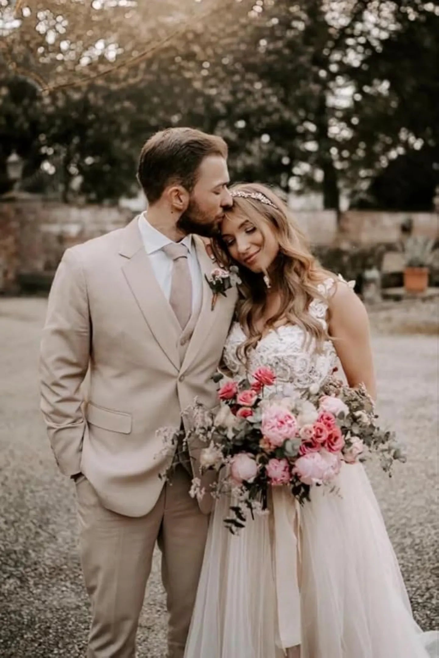 groom in beige 3 piece wedding suit with bride in lace dress at outdoor ceremony