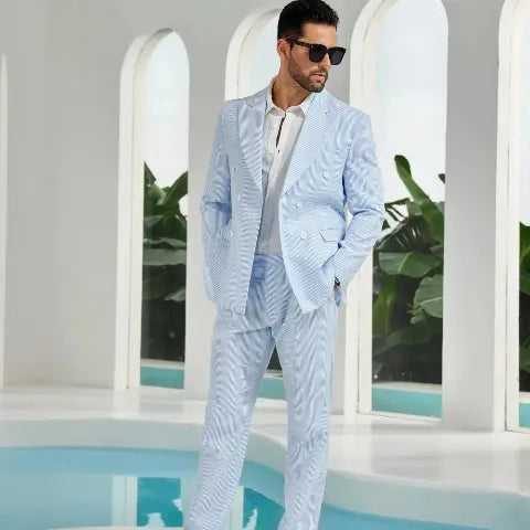 Relaxed man in a light-blue striped casual suit and sunglasses standing poolside, giving off an effortless resort vibe.