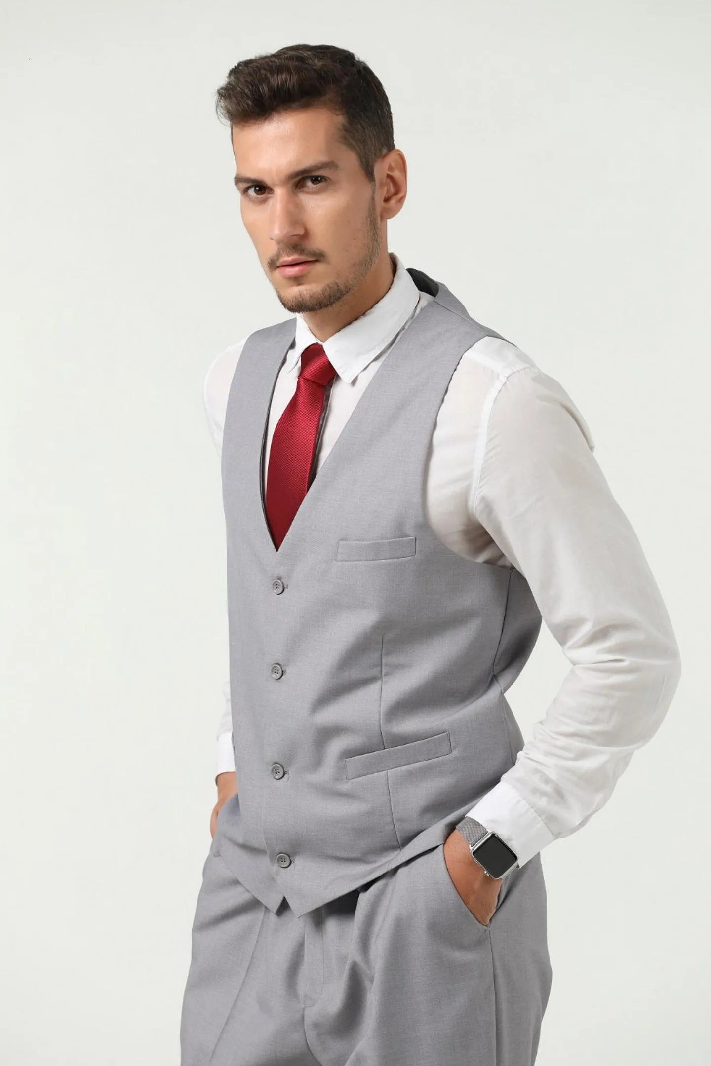 side view of man in grey slim fit vest, three-piece suit with red tie, hands in pockets for business wear.