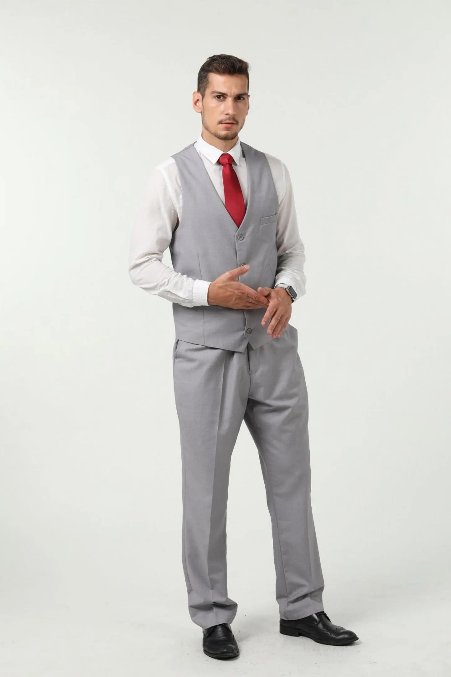model in grey three-piece suit vest with red tie, showing front view with hands in pockets.