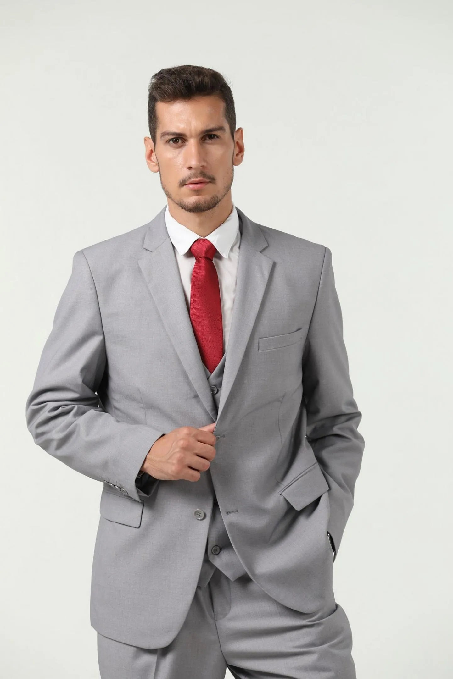 close-up of man in grey slim fit two-button 3-piece suit, holding the jacket with one hand and wearing a red tie.