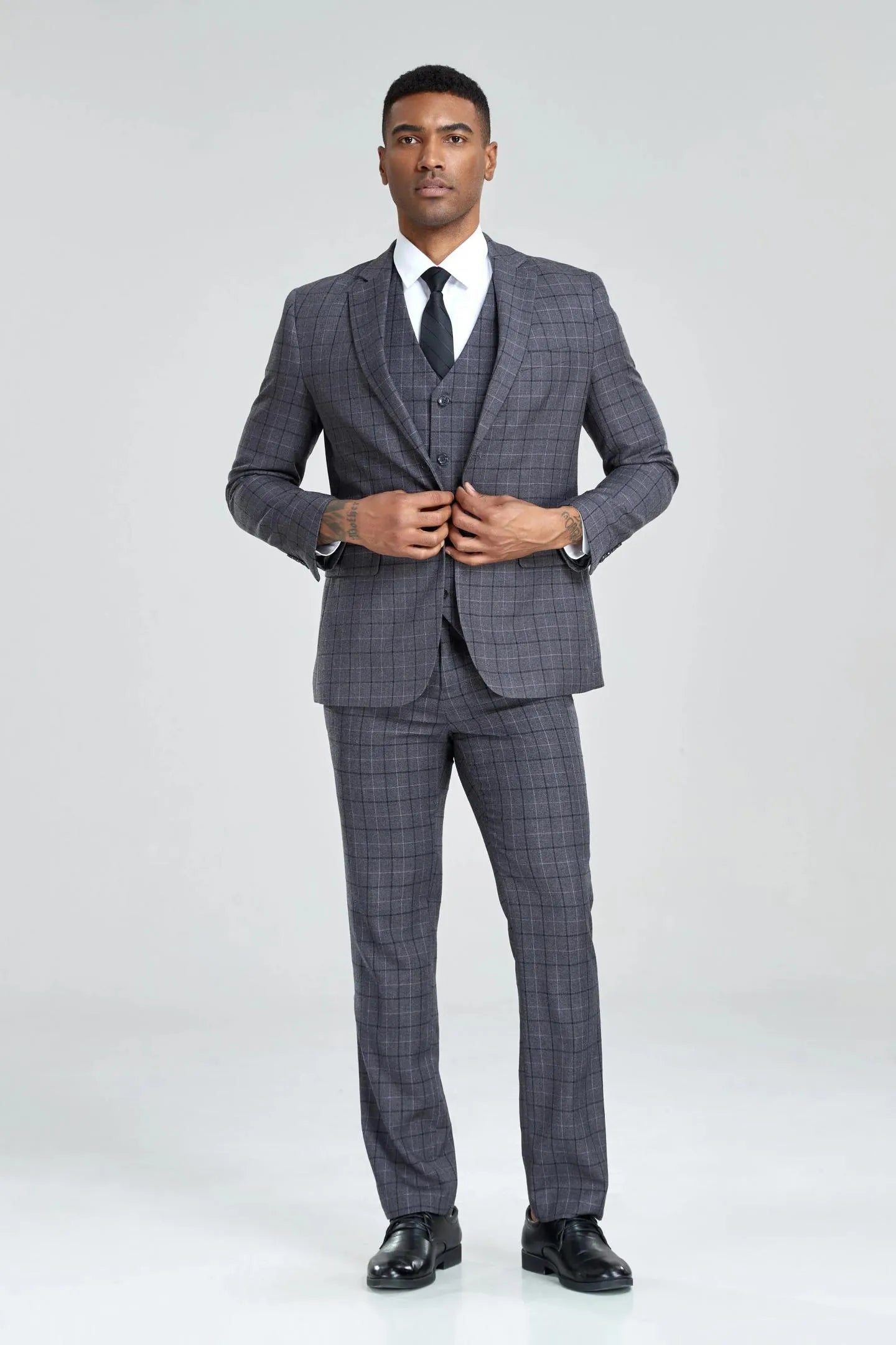 model in grey plaid 3-piece suit, front view, buttoning the jacket, red tie, business-formal look.