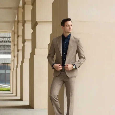 Elegant man in a light tan herringbone suit leaning against a column in a modern arcade, highlighting classic herringbone tailoring.