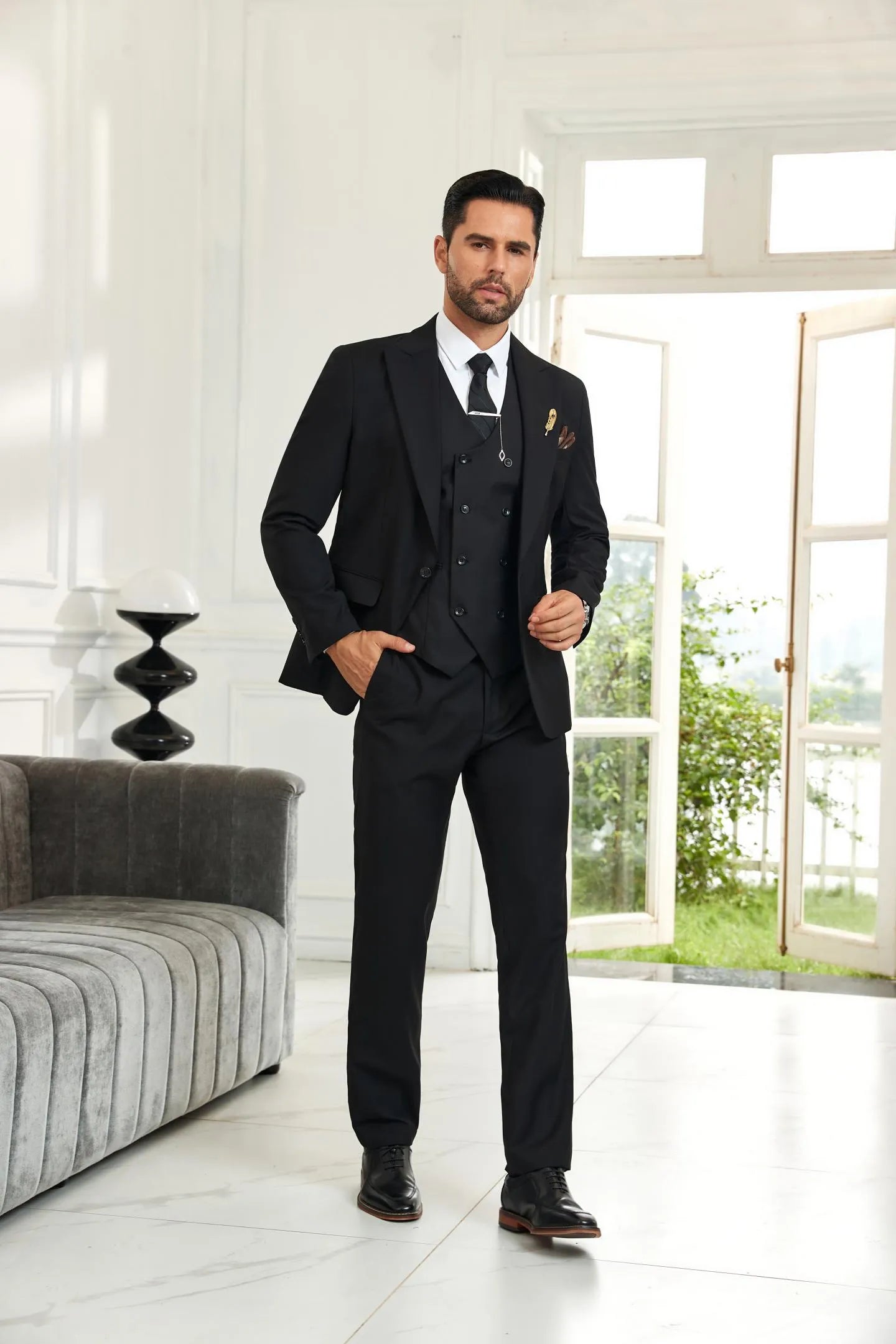 Model wearing black 3 piece men's suit with blazer, vest, and trousers in wedding formal style, front walking view.