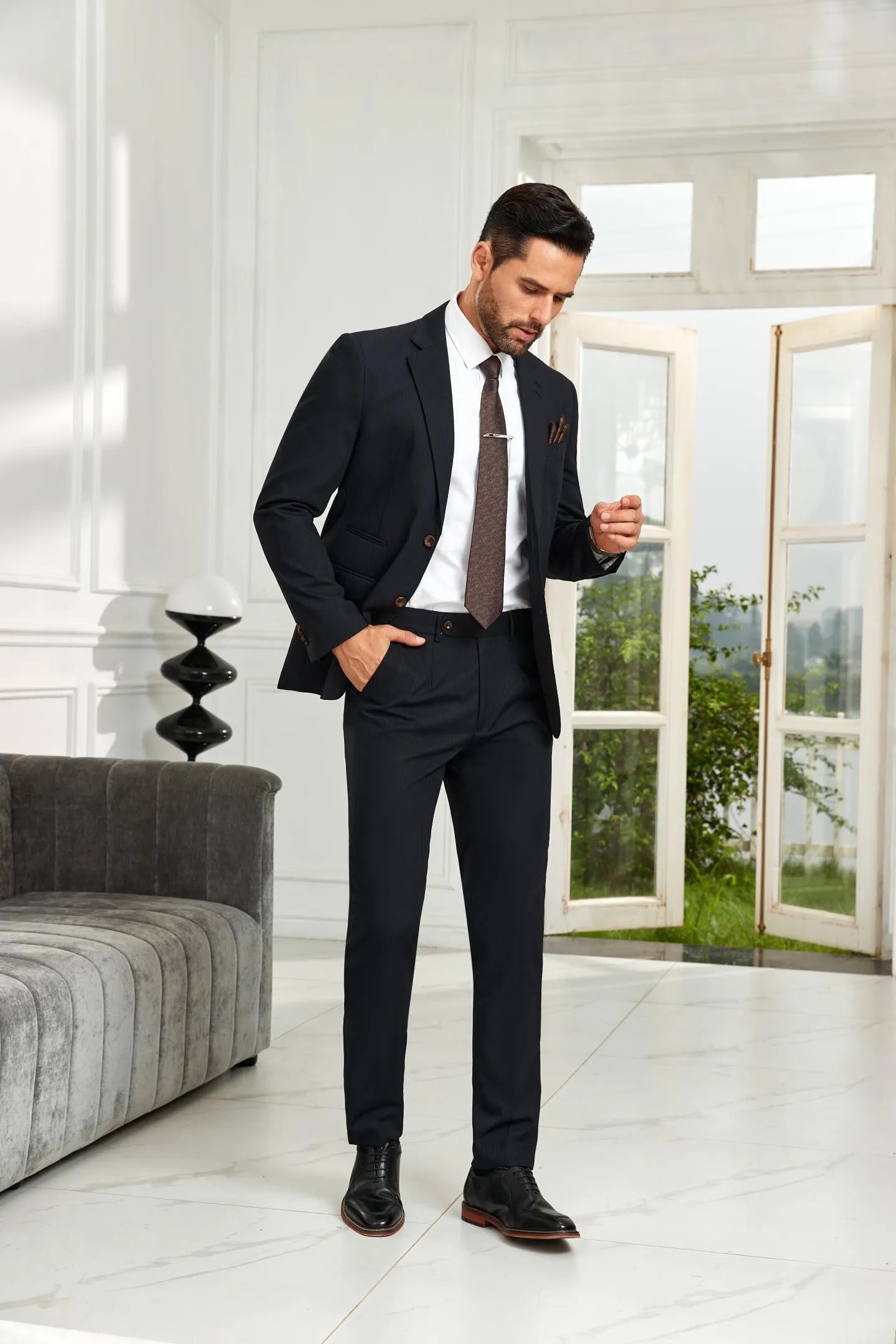 Model adjusting blazer in black striped 2 piece suit with brown tie and slim trousers, styled for modern business formal outfit