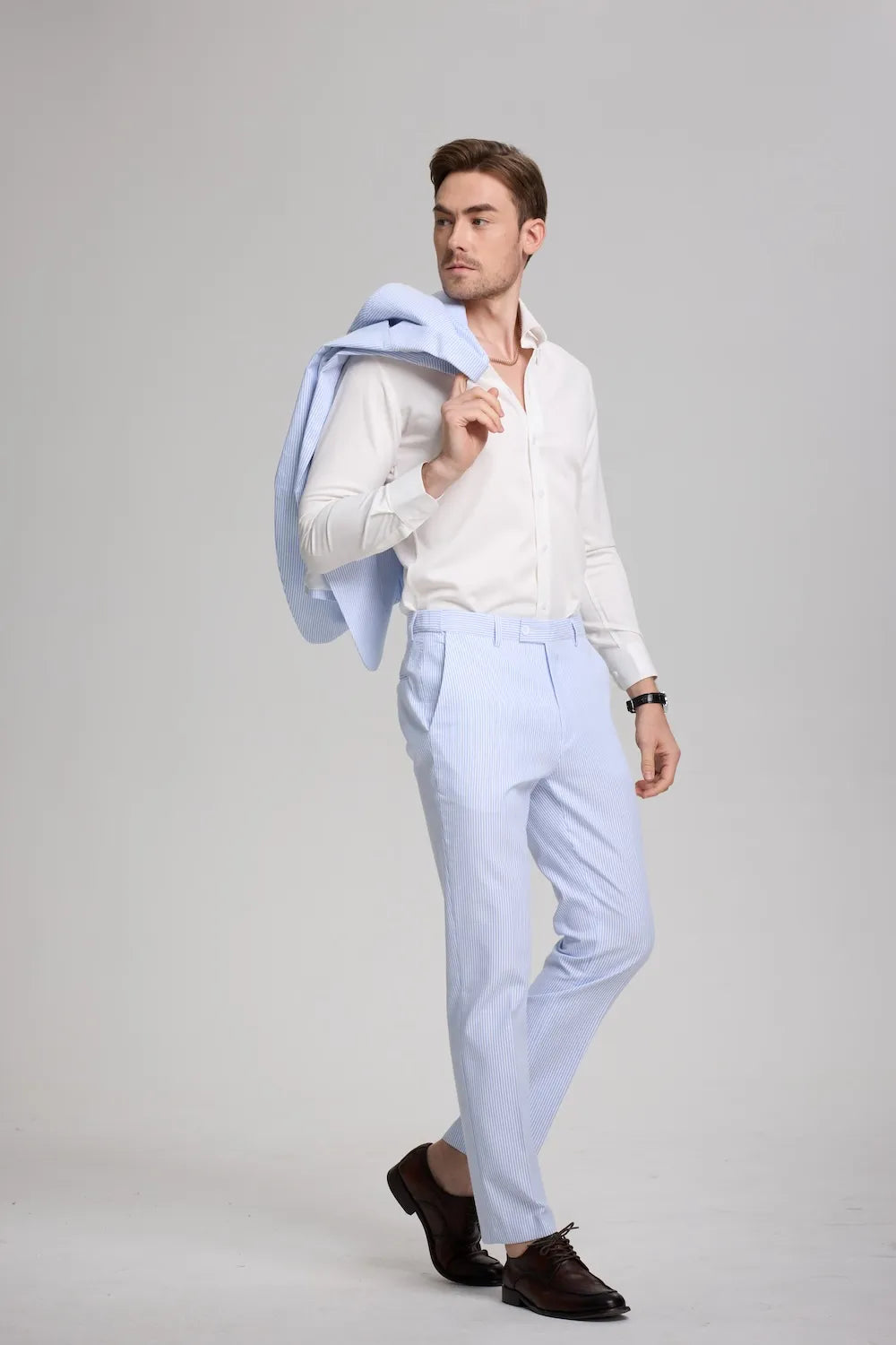 Man holding blue seersucker blazer over shoulder, wearing white shirt and pants
