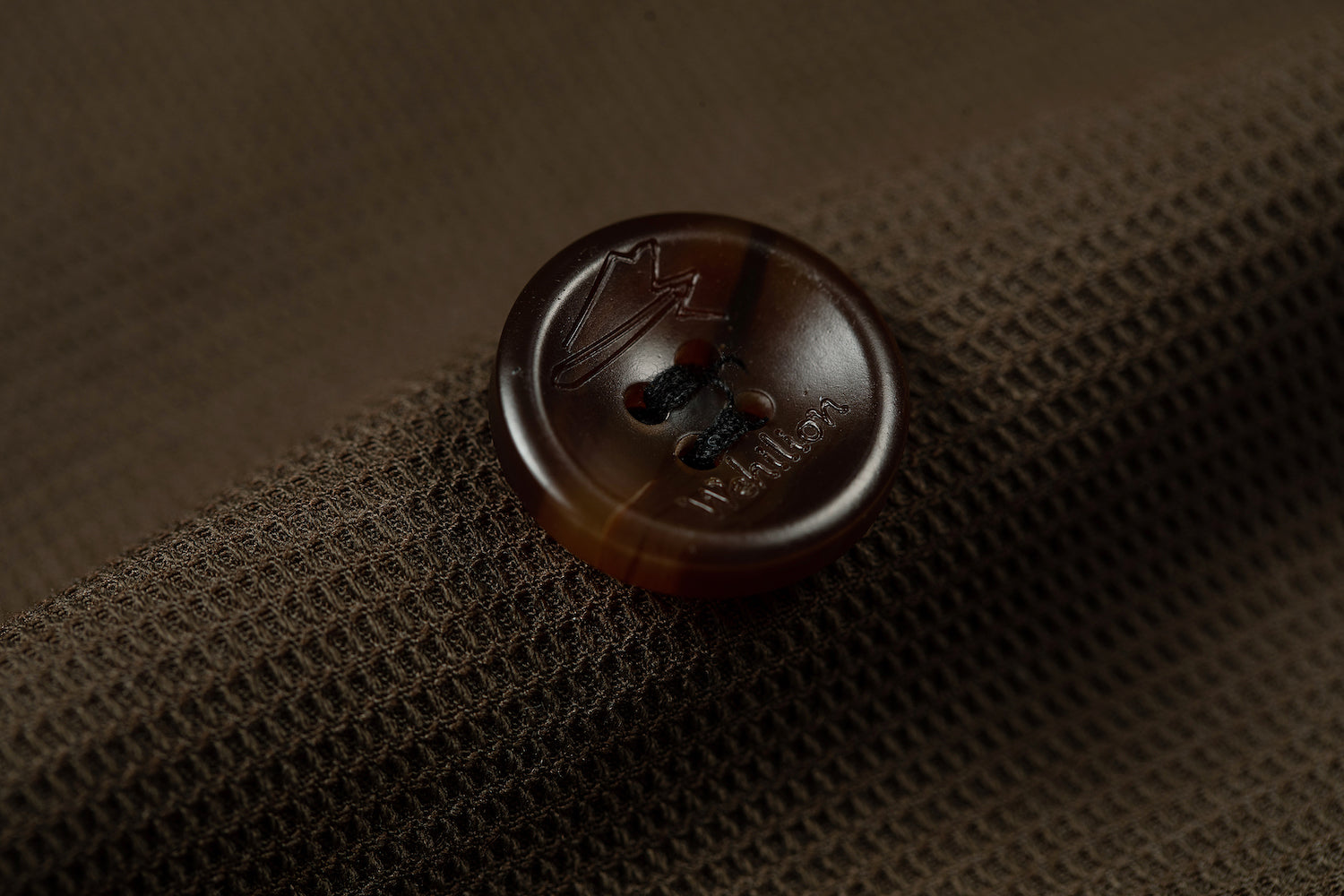 Designer brown double breasted blazer button close-up - horn button with engraved logo on textured fabric