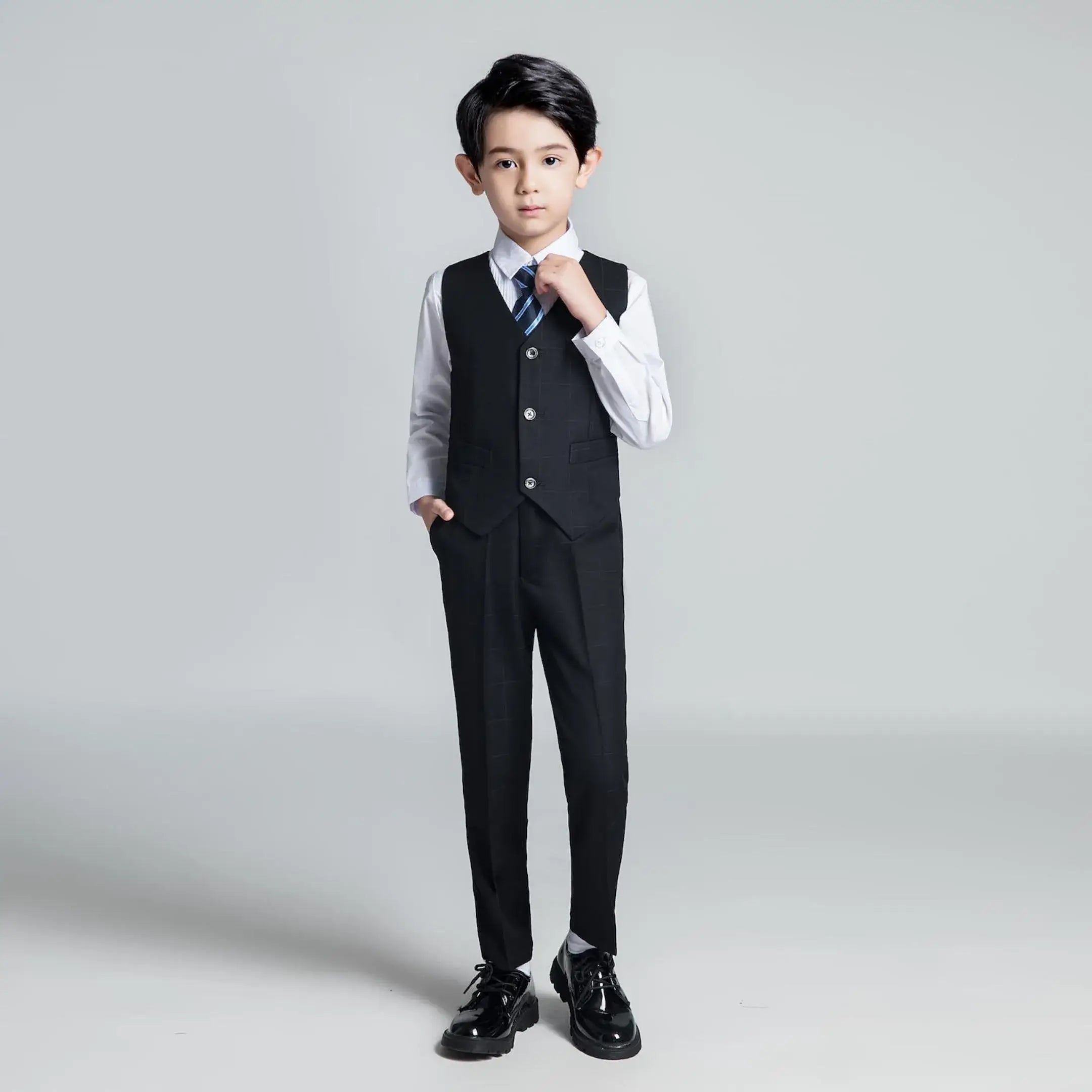 Boy in black plaid vest with striped tie and white shirt styled for formal occasions