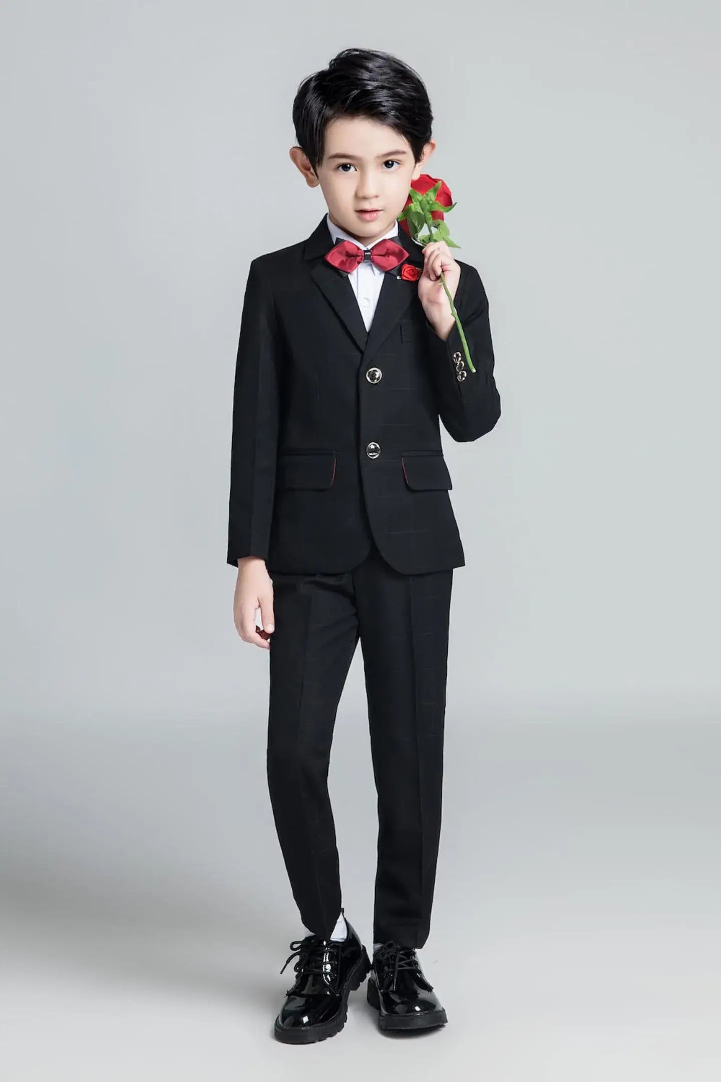 Young boy in black plaid tuxedo with red bow tie and rose, dressed for formal event