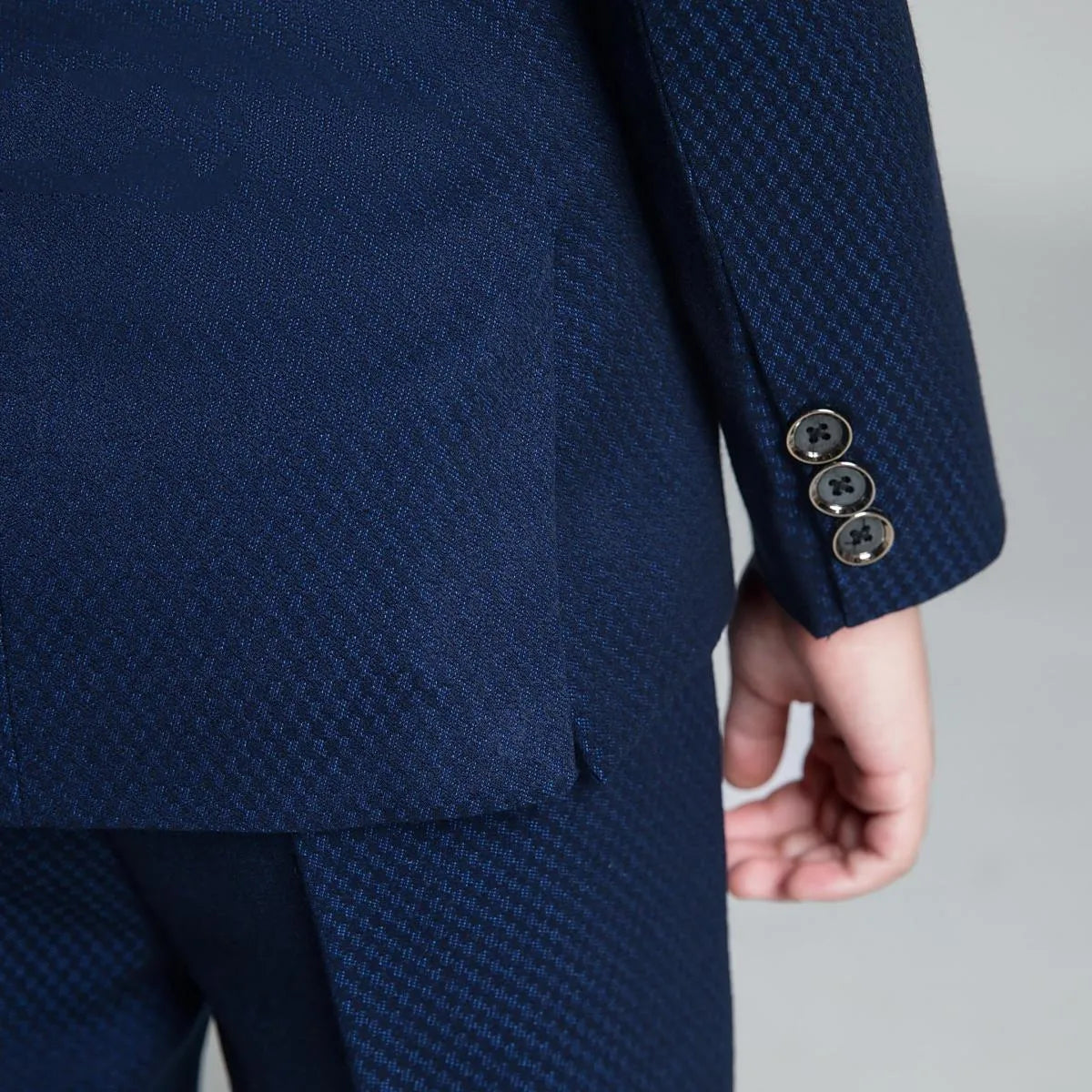 Detailed view of navy formal boys' suit sleeve with button accents and textured fabric for special occasions