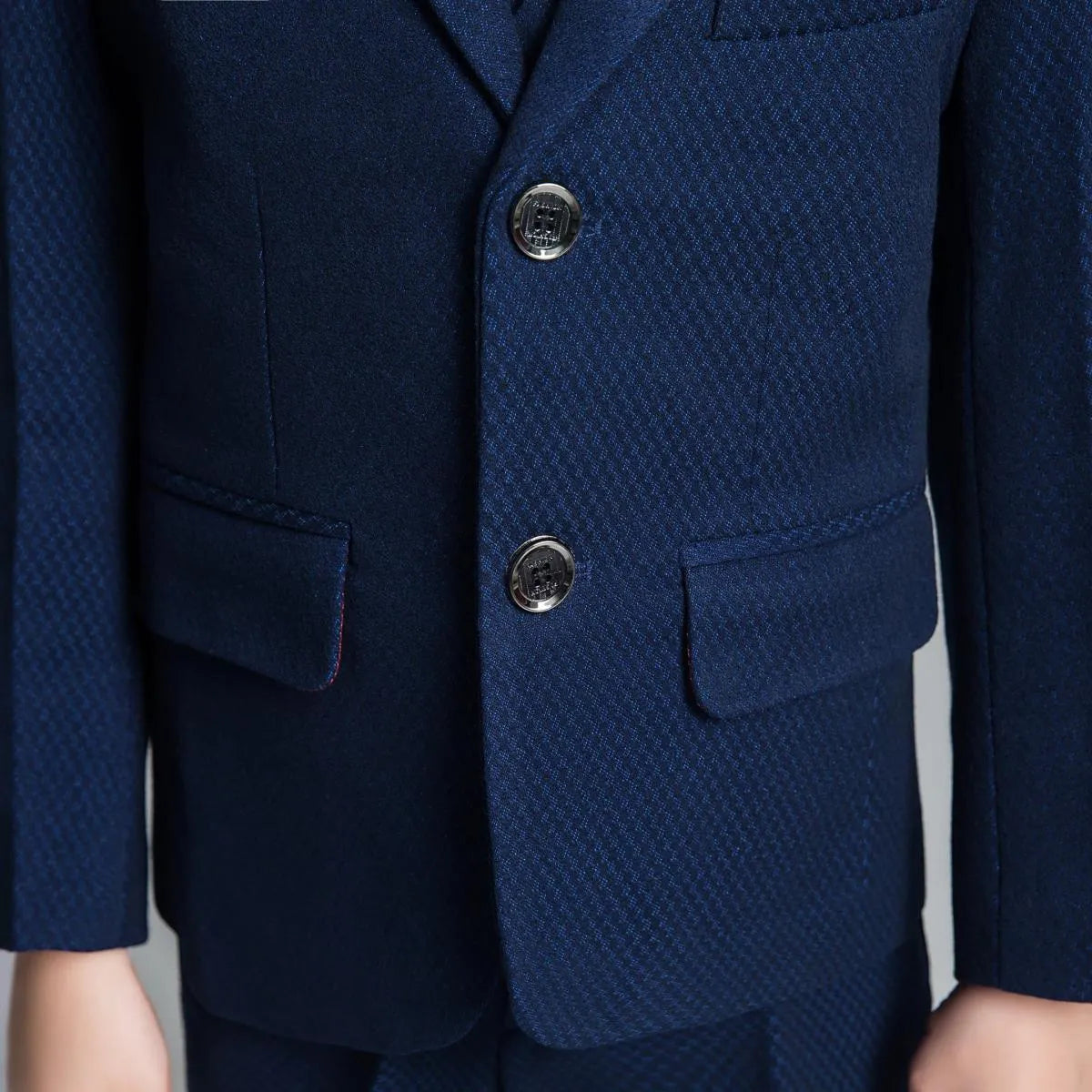 Close-up of navy boys' suit jacket with flap pockets, silver buttons, and fine textured weave for formal events